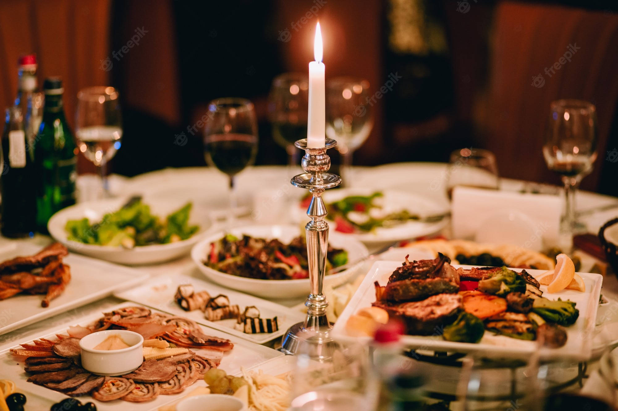蠟燭 桌布 壁紙 — 一張溫暖照明的餐桌，擺放著美食餐盤、酒杯和一個發光的燭台作為中心裝飾。