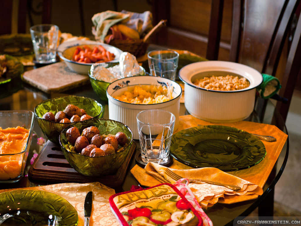 Food Table 桌布 壁紙 — 一張溫暖照明的餐桌上擺滿了色彩繽紛的食物碗，包括肉丸、馬鈴薯泥和玉米麵包，背景是木椅。