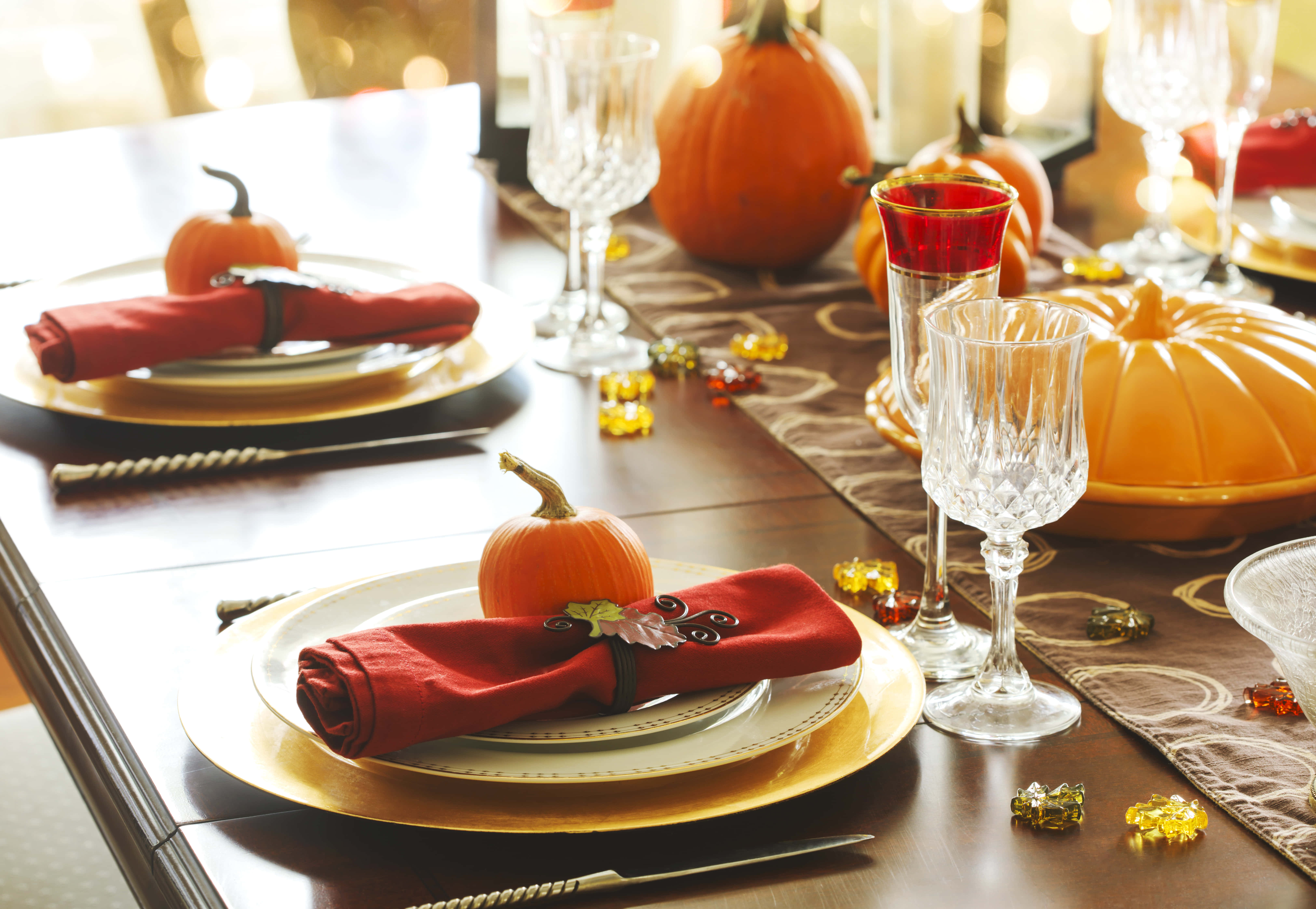Fall Thanksgiving 桌布 壁紙 — 一張溫暖燈光的秋季餐桌，擺放著橙色南瓜、紅色餐巾、金色盤子和水晶杯，營造節日晚餐氛圍。