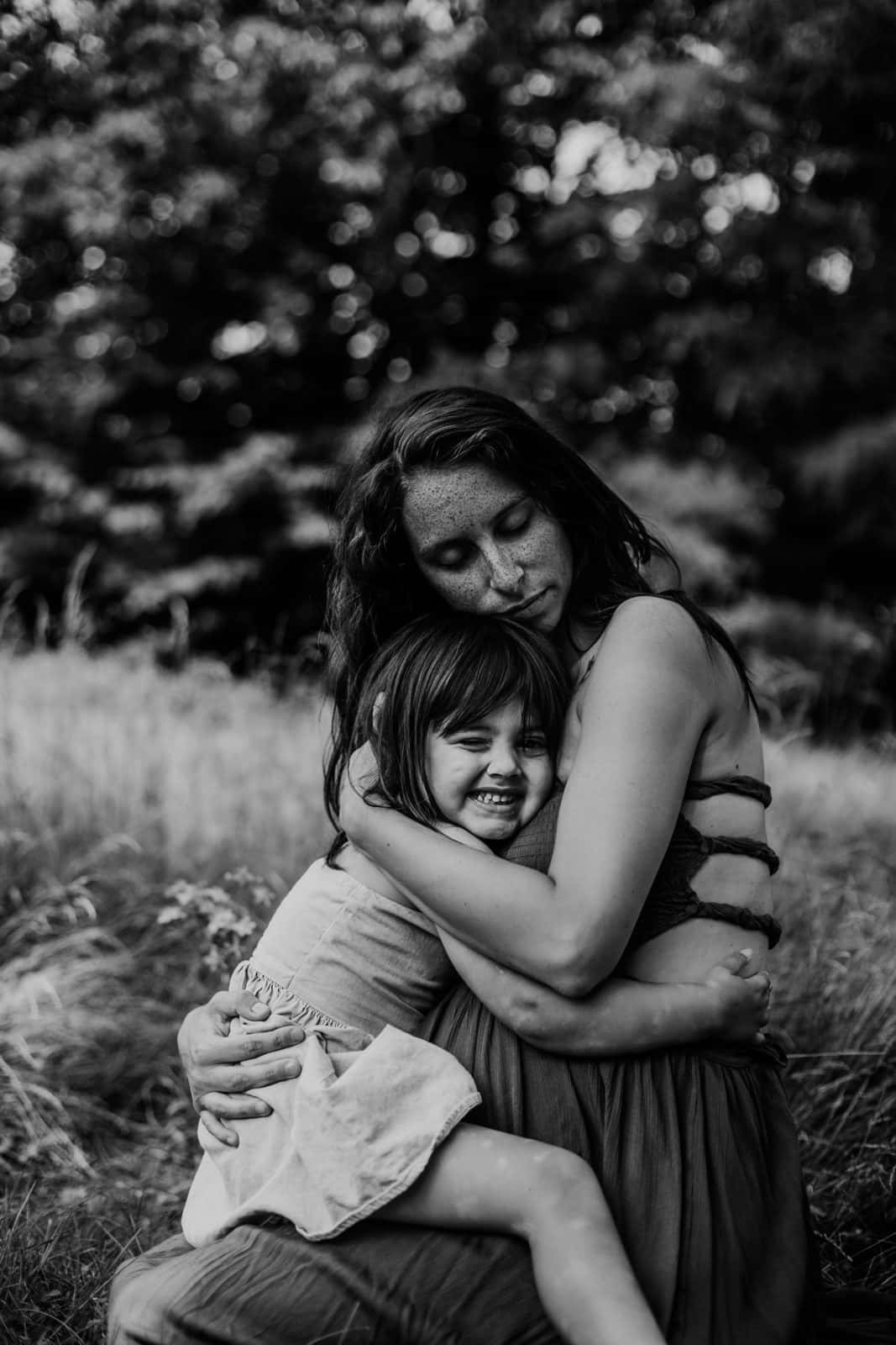 Mother Love 桌布 壁紙 — 一張溫柔的黑白照片，一位女士在陽光明媚的草地上擁抱著微笑的孩子，身後是模糊的樹木。