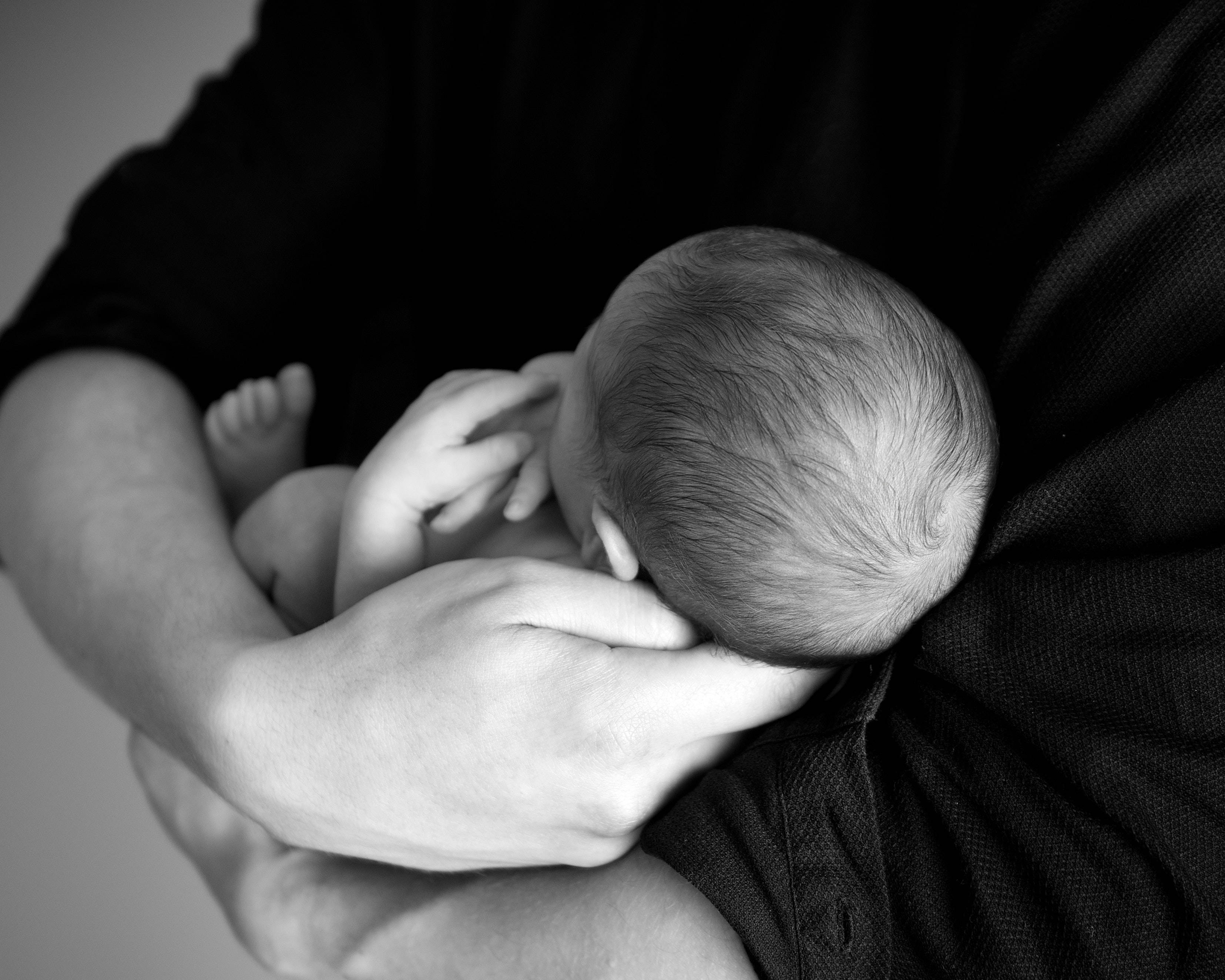 Newborn 桌布 壁紙 — 一張溫柔的黑白特寫，新生嬰兒在成人懷中安詳入睡。