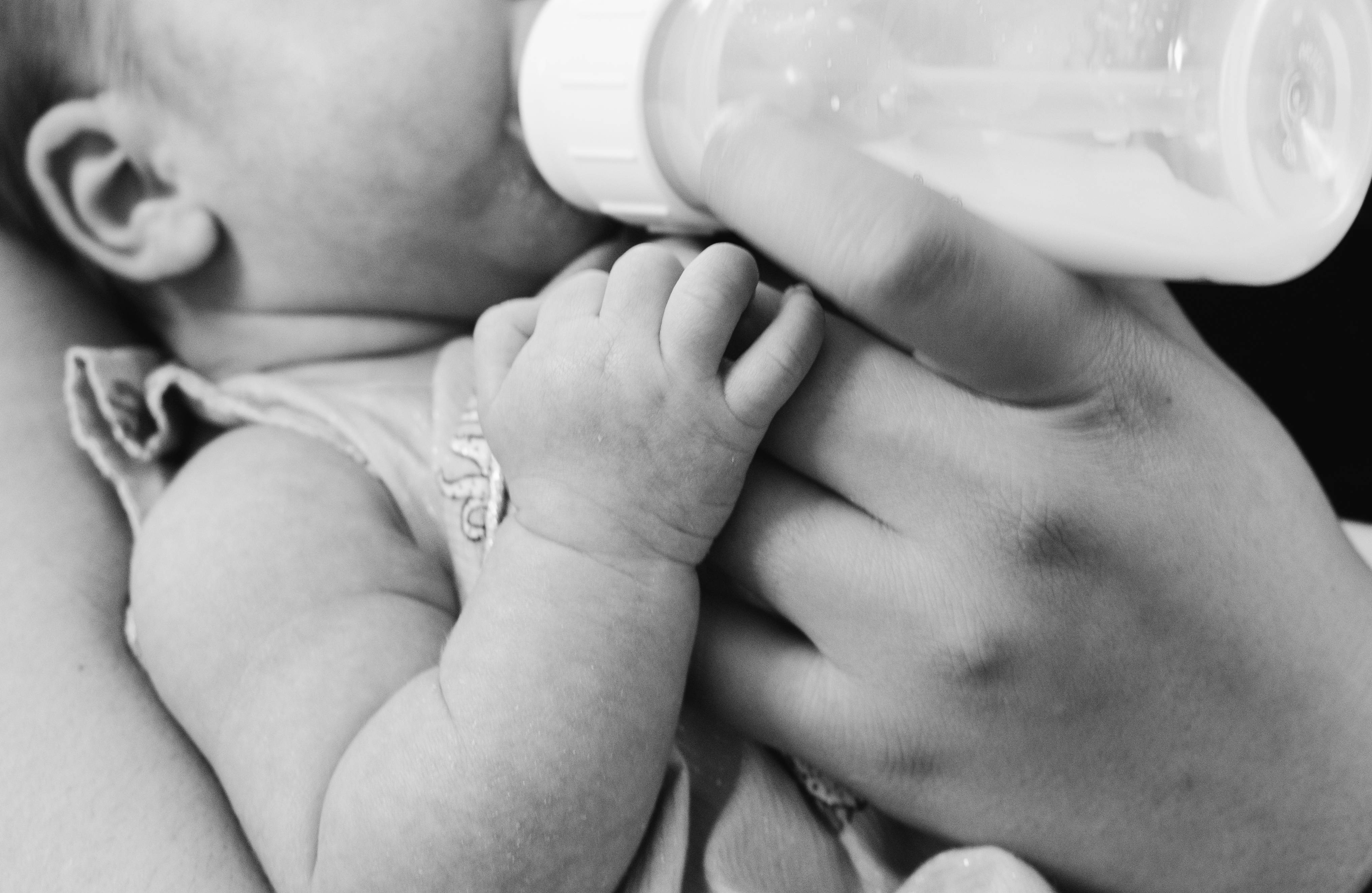 Baby Boy 桌布 壁紙 — 一張溫柔的黑白特寫，顯示嬰兒被成人手抱著喝奶瓶。