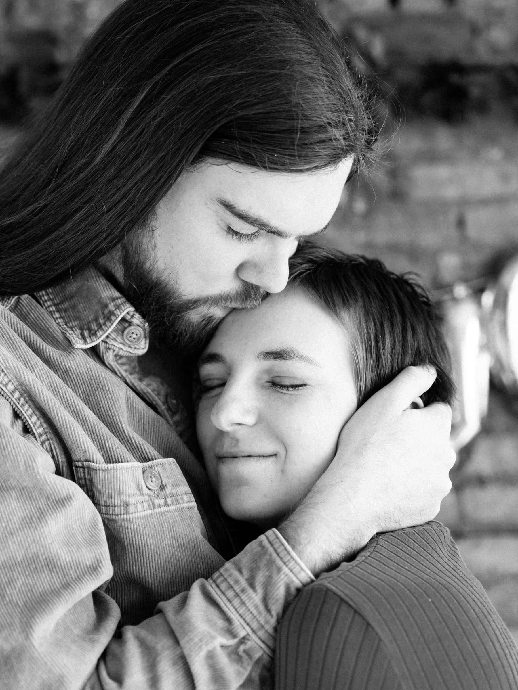 Forehead Kiss 桌布 壁紙 — 一張溫柔的黑白肖像，男人輕吻女人的額頭，而她將頭靠在他的胸膛上。