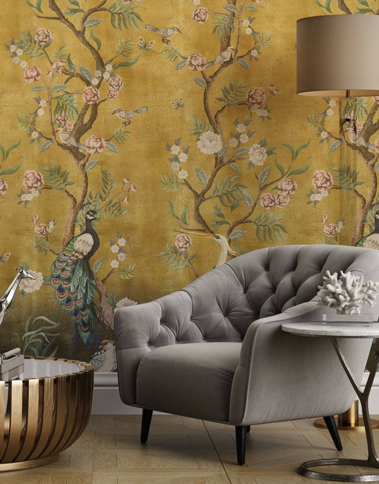 Chinoiserie 桌布 壁紙 — 一張灰色簇絨扶手椅放在金色壁紙前，壁紙飾有孔雀和開花的樹木。