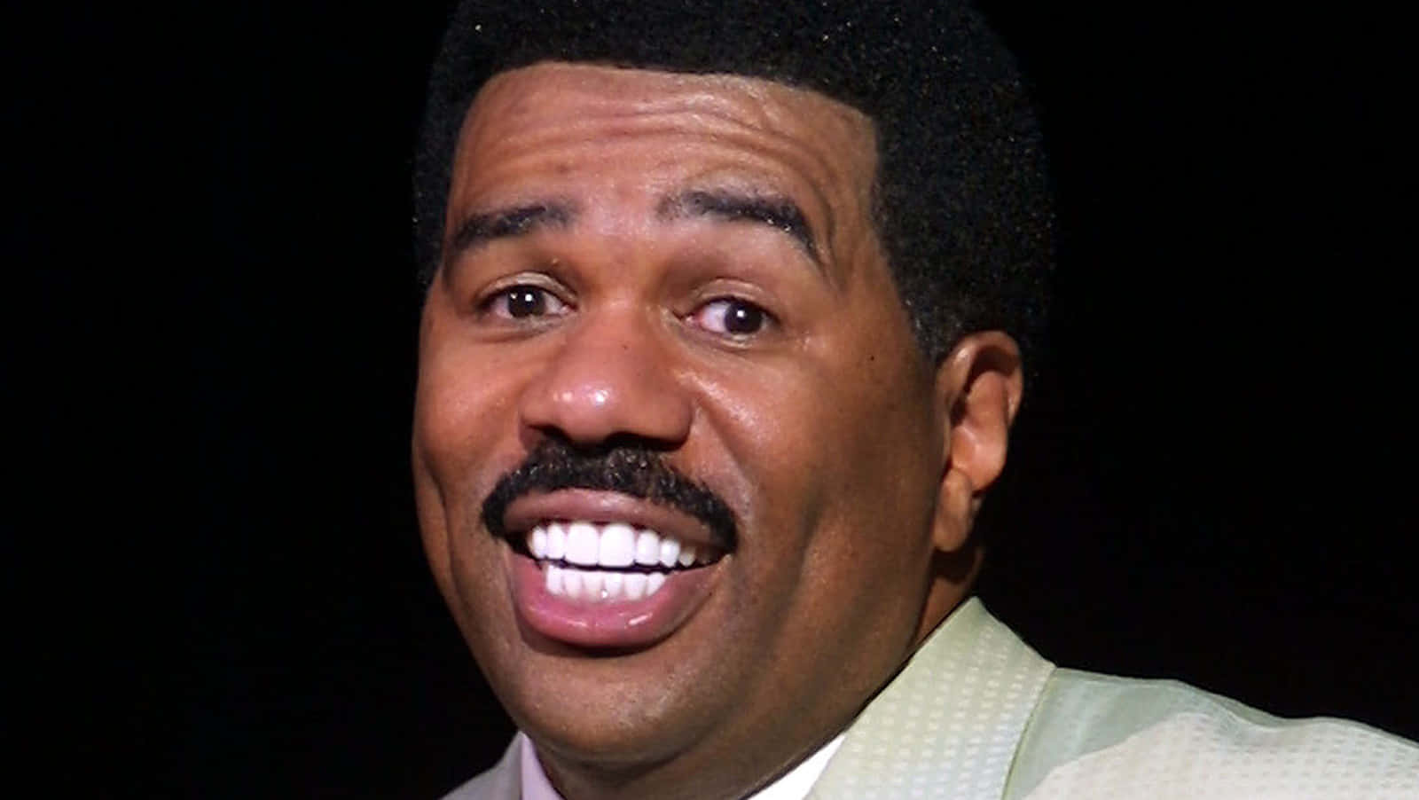 steve harvey 桌布 壁紙 — 一張特寫照片，一名留鬍鬚的微笑男子穿著淺綠色西裝，背景為黑色。