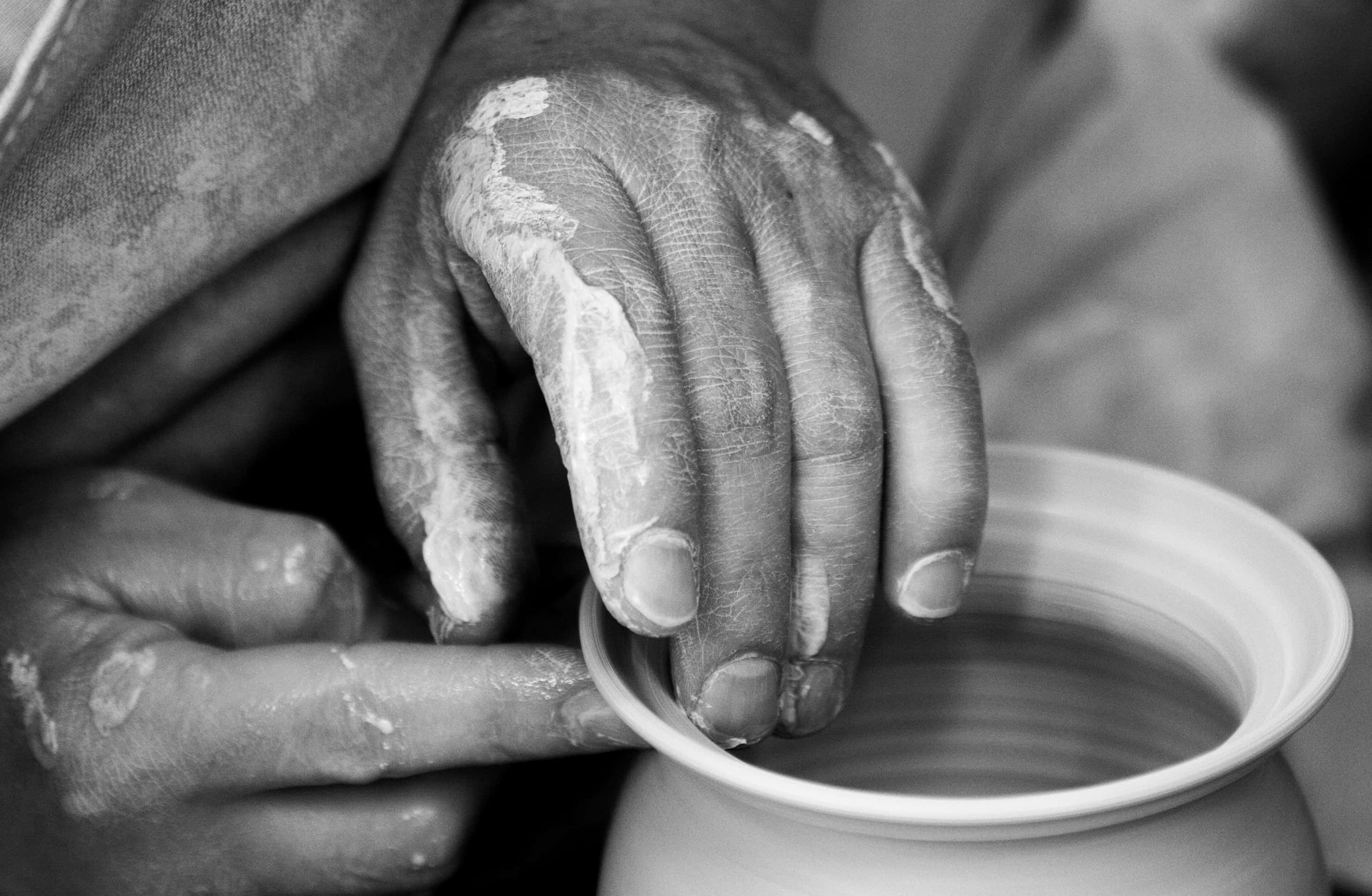 hands 桌布 壁紙 — 一張特寫黑白照片，展示一雙飽經風霜的手在陶輪上塑造濕黏土。