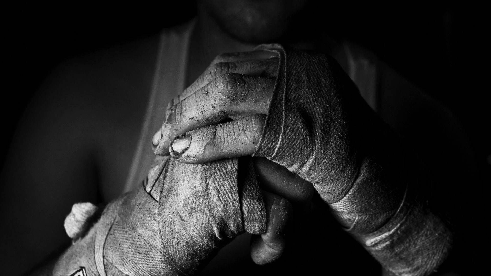 Boxing 桌布 壁紙 — 一張特寫黑白照片，拍攝一名拳擊手的手緊緊包裹在破舊的皮手套中，背景為深色。