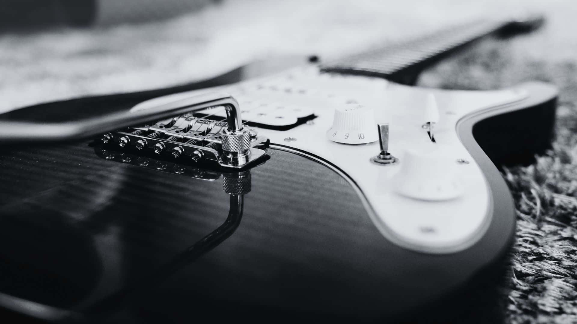 Black And White Guitar 桌布 壁紙 — 一張特寫黑白照片，拍攝一把時尚的電吉他放在有紋理的地毯上，焦點銳利地落在其琴橋和旋鈕上。