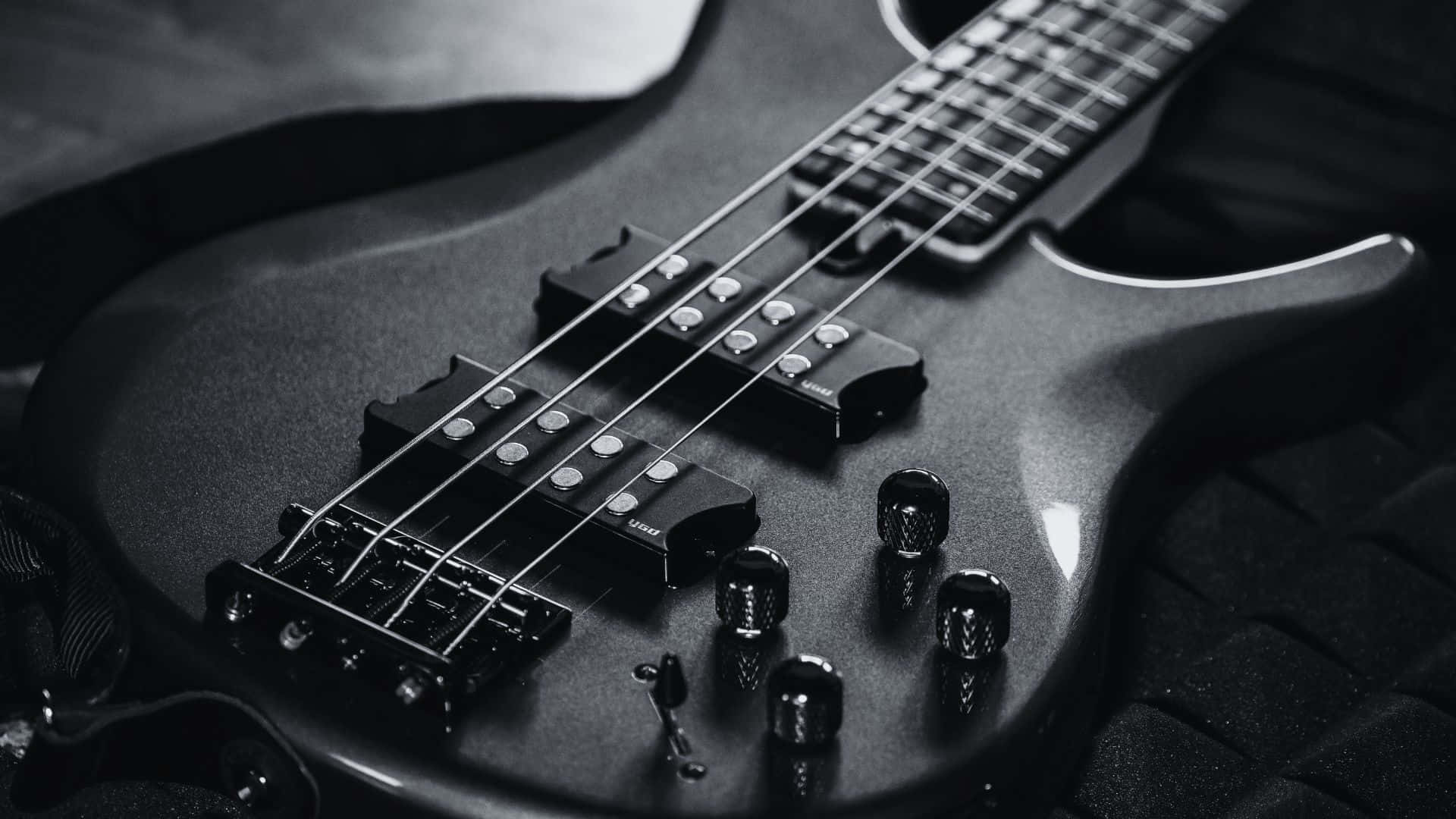 Black And White Guitar 桌布 壁紙 — 一張特寫黑白照片，拍攝一把時尚的低音吉他放在有紋理的表面上，焦點銳利對準其弦線和旋鈕。