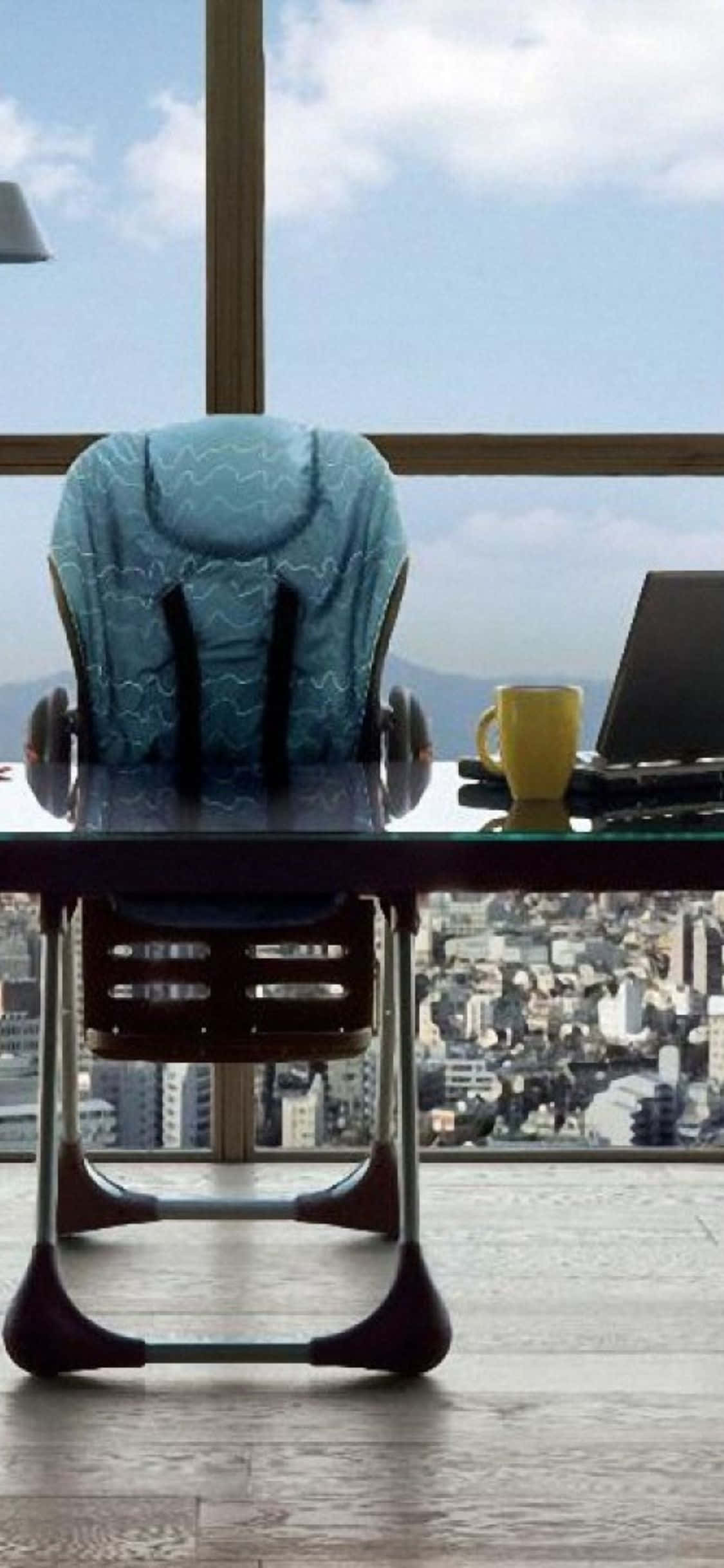 iPhone Xs Desk 桌布 壁紙 — 一張現代人體工學椅放在玻璃桌前，俯瞰著廣闊的城市景觀，天空湛藍，白雲朵朵。