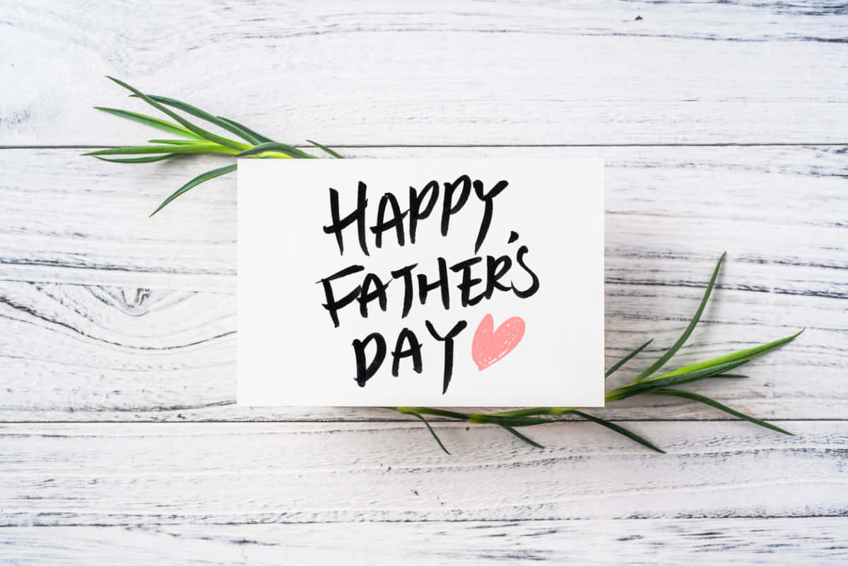 Fathers Day 桌布 壁紙 — 一張白色卡片，上面有手寫的「HAPPY FATHER'S DAY」和一個粉紅色的心形，放在白色木板上，配以綠色的迷迭香枝。