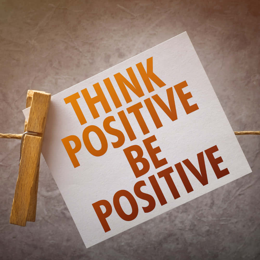 激勵 桌布 壁紙 — 一張白色卡片，上面有粗體橙色文字「THINK POSITIVE BE POSITIVE」，用衣夾掛在麻繩上，背景為有紋理的棕色。