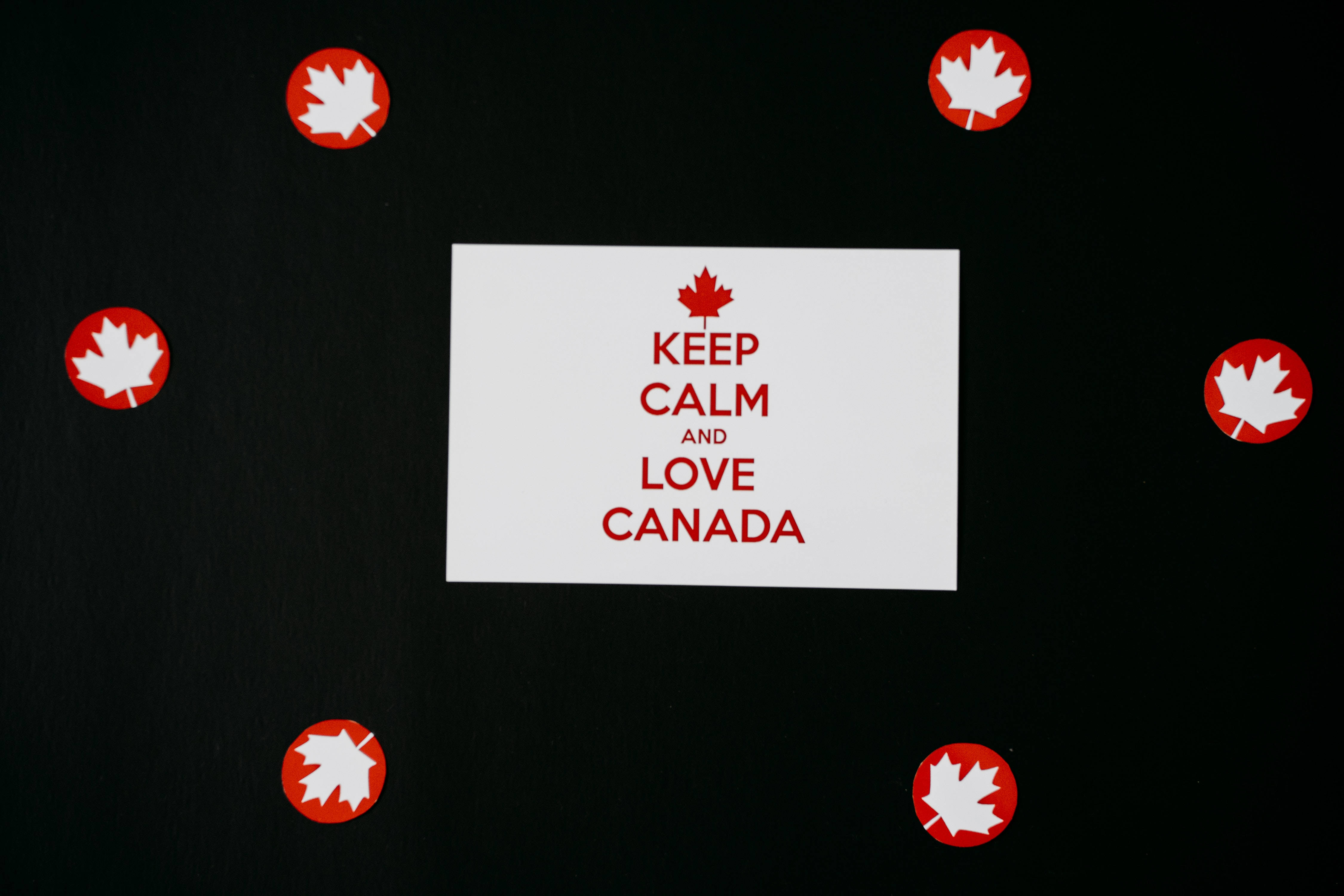 語錄 桌布 壁紙 — 一張白色卡片，上面有紅色文字寫著「KEEP CALM AND LOVE CANADA」，周圍是紅色楓葉貼紙，放在黑色表面上。