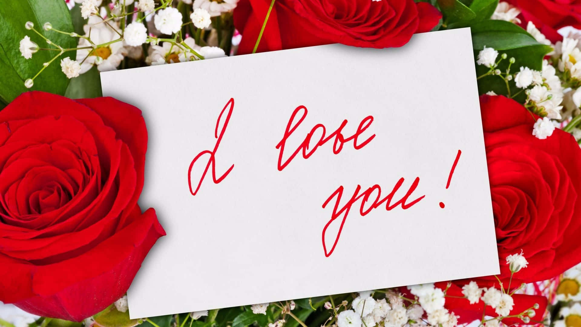 love you 桌布 壁紙 — 一張白色卡片，上面有紅色草書文字寫著「我愛你！」，依偎在鮮豔的紅玫瑰和精緻的白色滿天星中。
