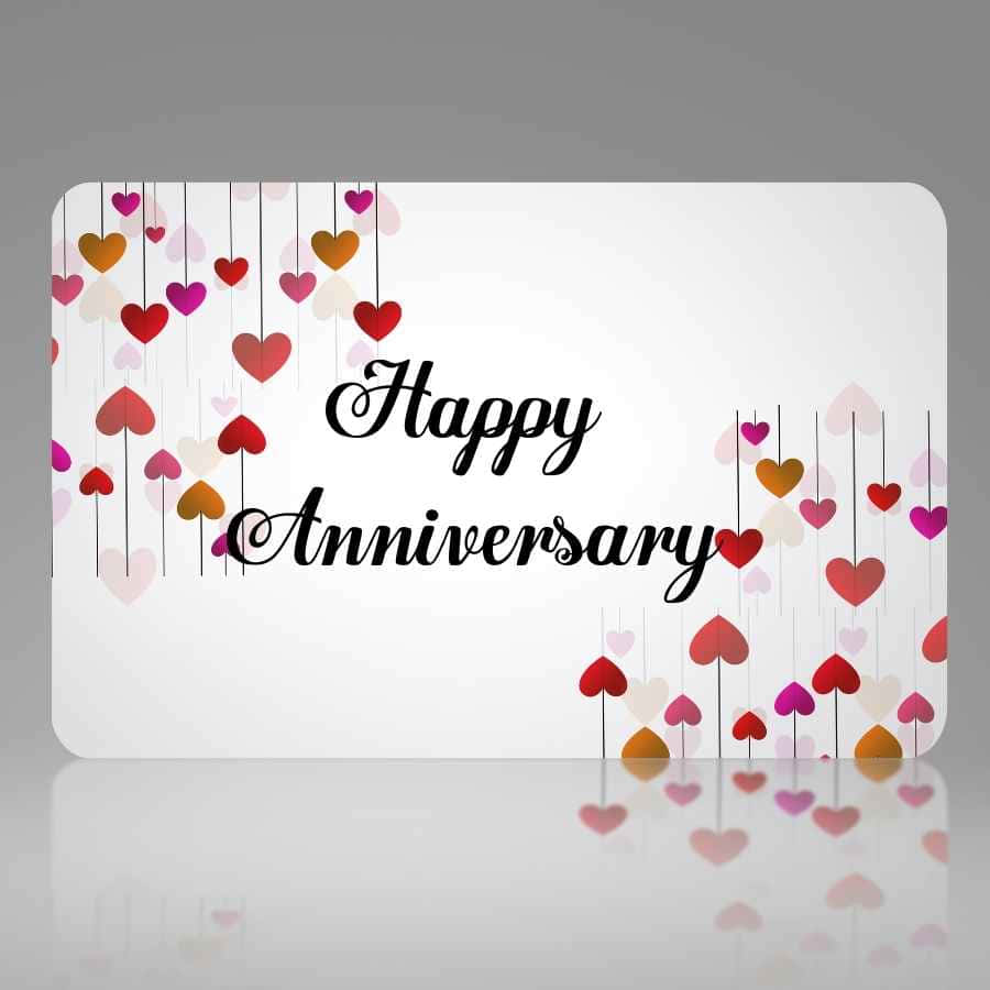 Anniversary 桌布 壁紙 — 一張白色卡片，上面用黑色草書寫著「Happy Anniversary」，周圍掛滿彩色心形裝飾，置於灰色反光表面上。