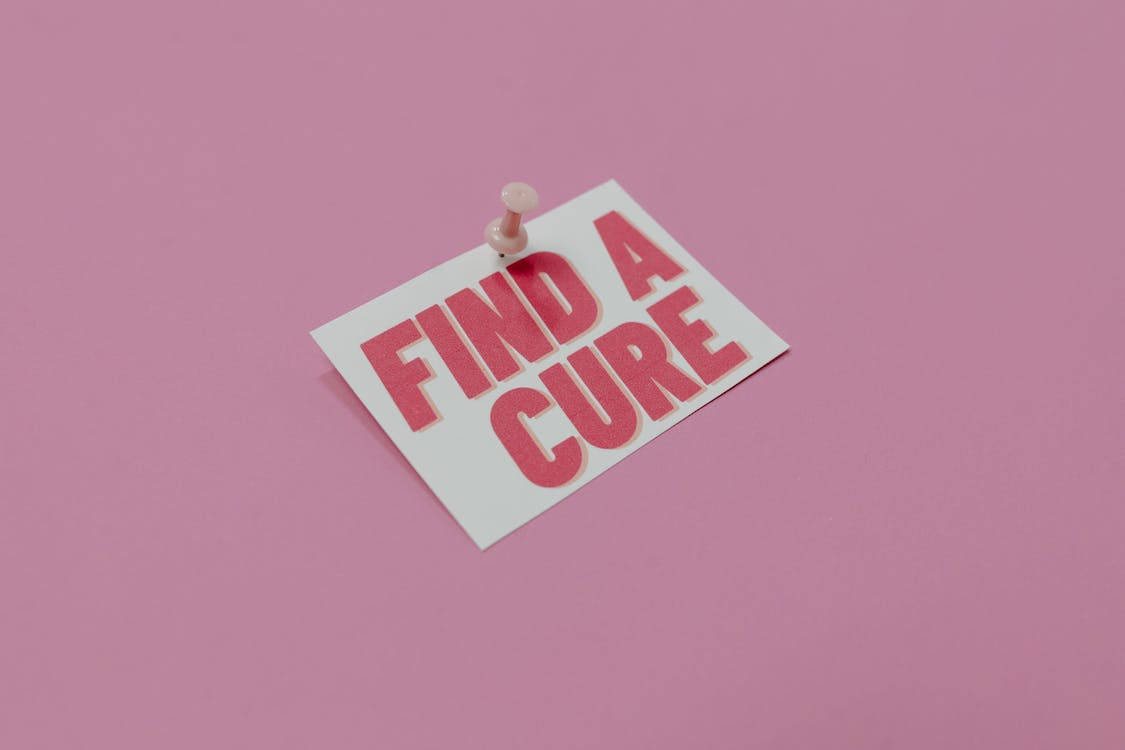 粉紅色 桌布 壁紙 — 一張白色卡片上以粗體紅色文字寫著「FIND A CURE」，被釘在純粉紅色背景上。