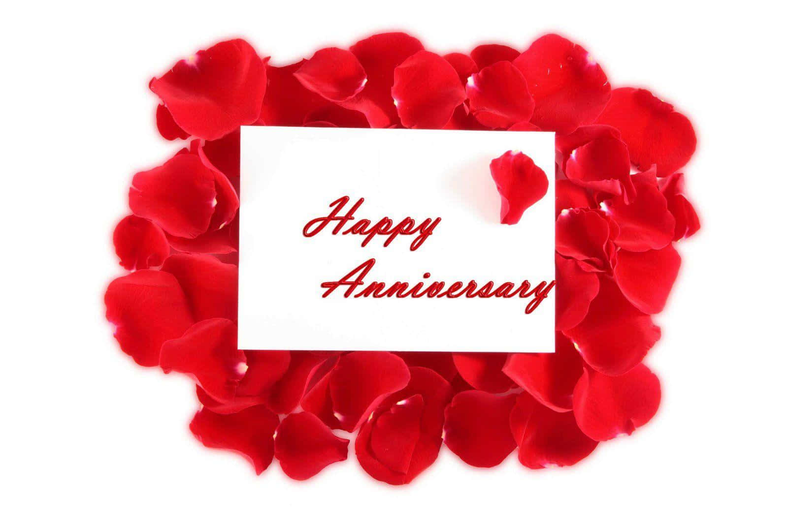 玫瑰美學 桌布 壁紙 — 一張白色卡片上以紅色草書寫著「Happy Anniversary」，周圍由鮮紅色玫瑰花瓣組成的愛心形狀環繞，背景為純白色。