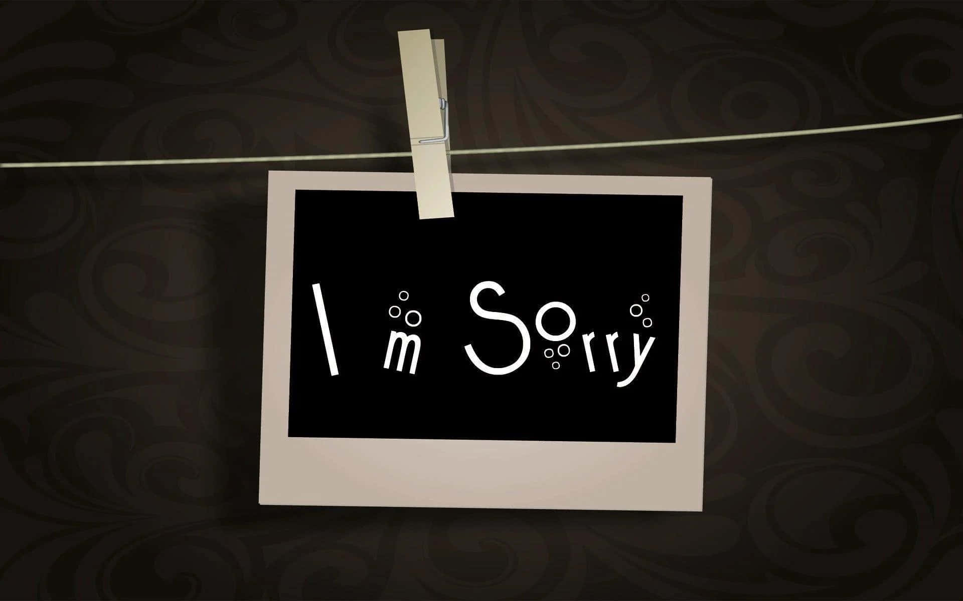 Sorry 桌布 壁紙 — 一張白色拍立得照片，上面有 'I'm Sorry' 的俏皮白色字體，用衣夾掛在電線上，背景是深色漩渦狀壁紙。