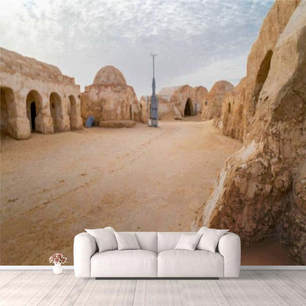 Tatooine 桌布 壁紙 — 一張白色沙發放在一幅巨大的壁紙前，壁紙描繪了沙質沙漠城鎮莫斯艾斯利，有圓頂建築和高天線，天空多雲。