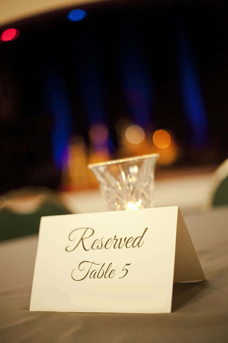 高清 桌布 壁紙 — 一張白色預留桌卡「Table 5」放在鋪有桌巾的桌子上，背景有水晶燭台和彩色散景燈光。