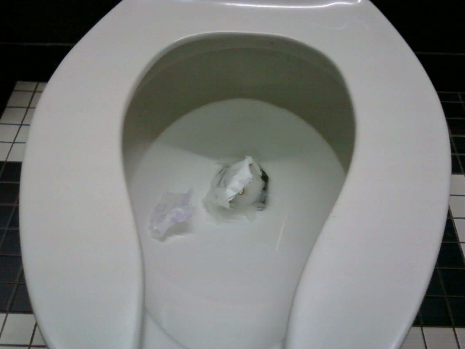 Embarrassing 桌布 壁紙 — 一張白色馬桶的特寫照片，有皺巴巴的衛生紙和一個塑膠包裝漂浮在水面上，背景是黑白瓷磚地板。