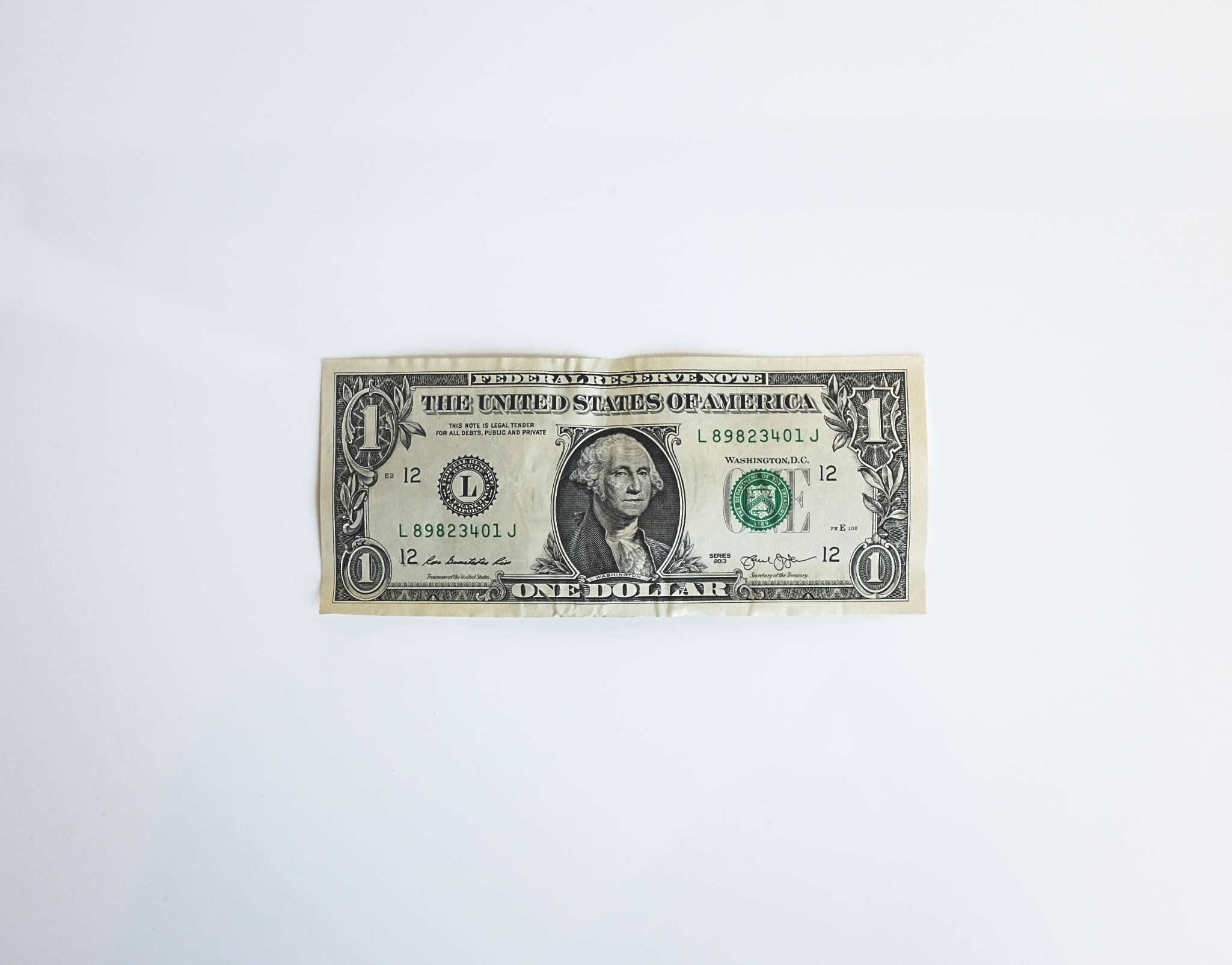 金錢 桌布 壁紙 — 一張皺巴巴的一美元紙鈔平放在純白色表面上，光線明亮均勻。