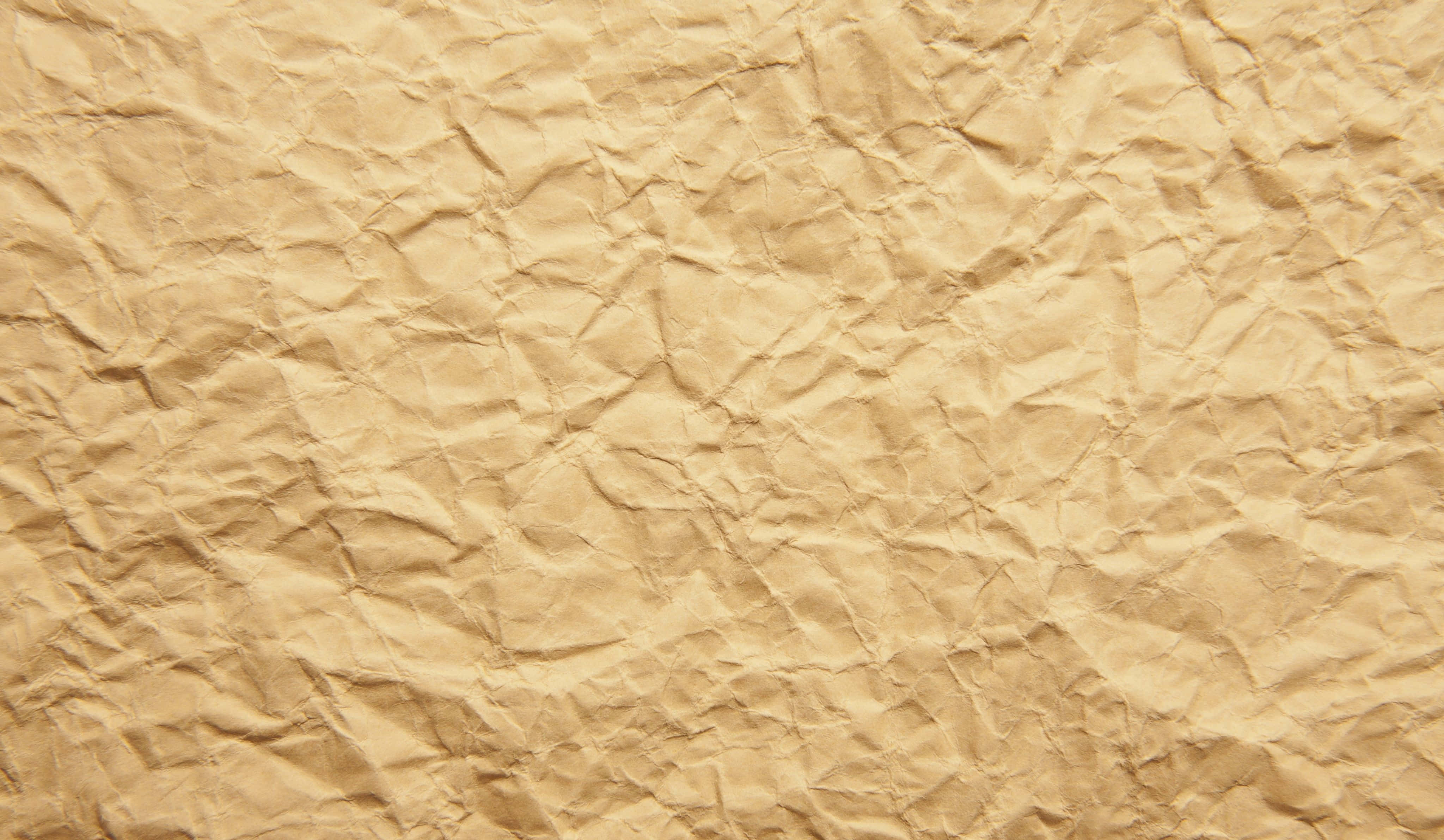 Brown Paper 桌布 壁紙 — 一張皺巴巴的米色紙張特寫，帶有複雜的摺痕和陰影，營造出觸感紋理。