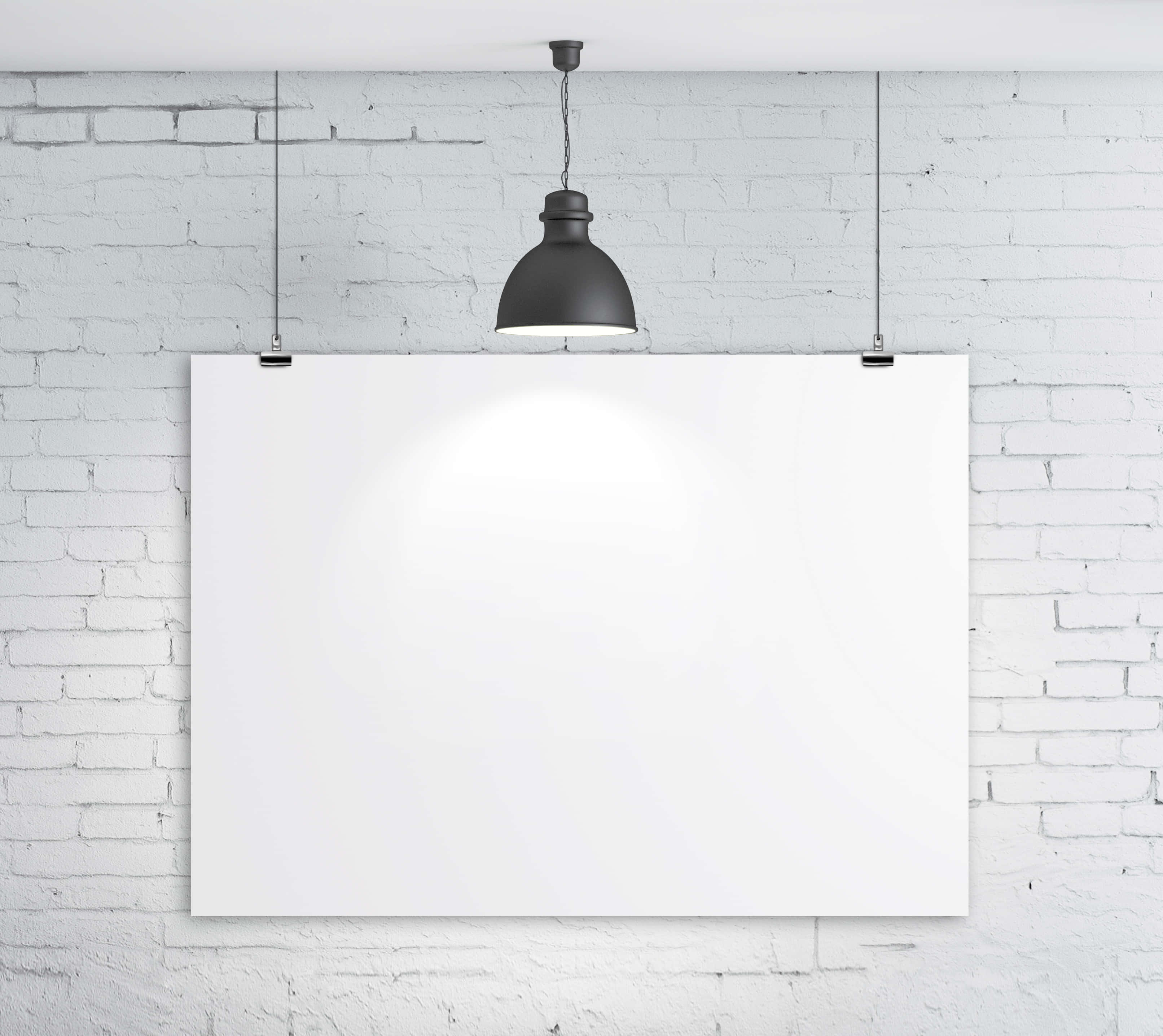 Poster Board 桌布 壁紙 — 一張空白白色海報掛在白色磚牆上，下方有一盞黑色吊燈投射出柔和的光芒。
