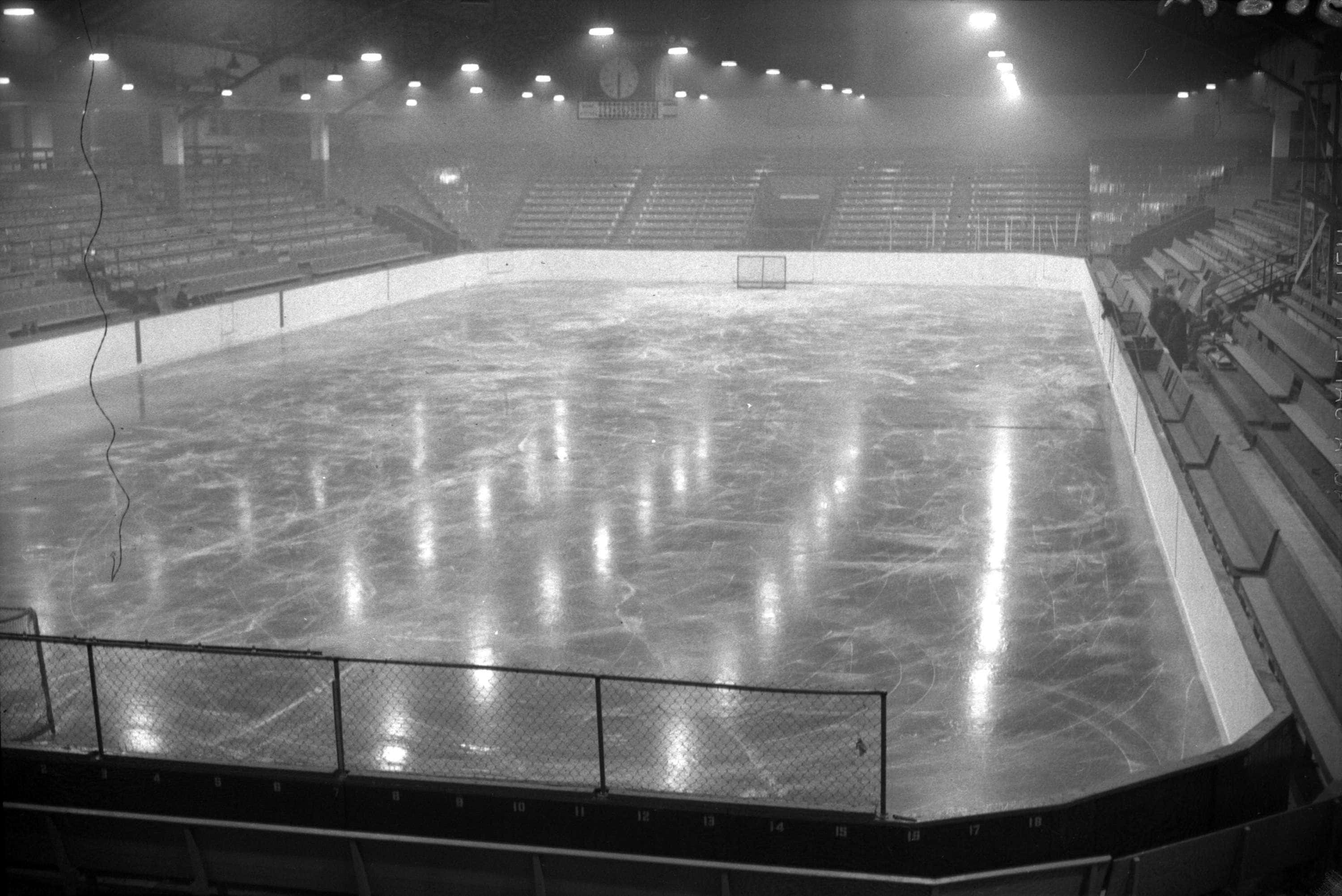 Ice Rink 桌布 壁紙 — 一張空蕩蕩的溜冰場黑白照片，裂開的冰面反射著天花板的燈光及空無一人的看台。