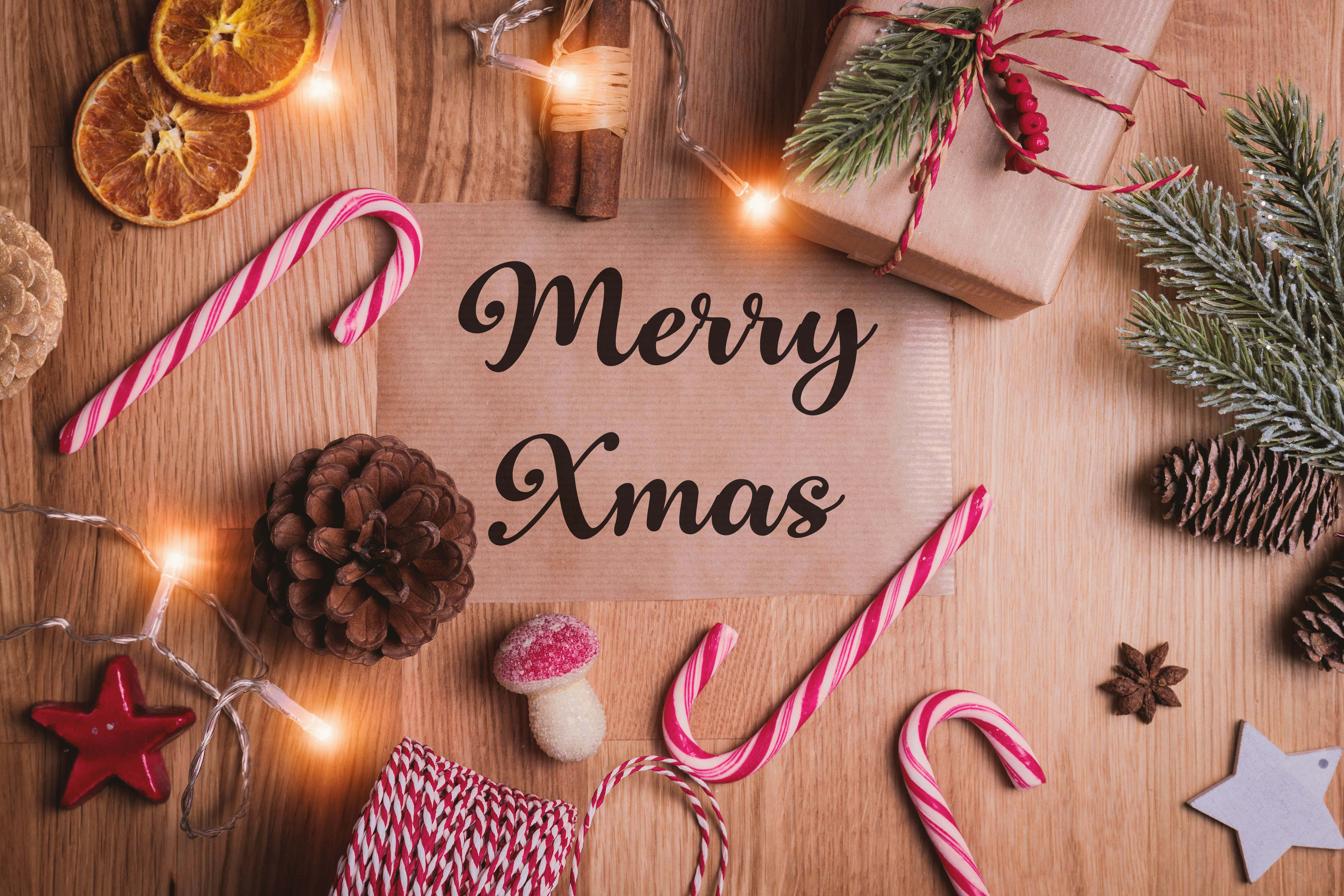 Festive 桌布 壁紙 — 一張節日木桌，上面裝飾著拐杖糖、松果、燈飾和一個「Merry Xmas」標誌，周圍環繞著節日裝飾。