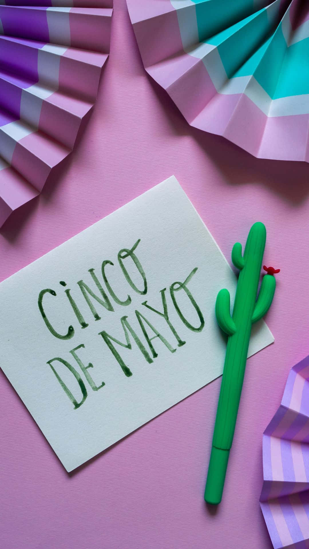 Cinco De Mayo 桌布 壁紙 — 一張節日氣氛濃厚的 Cinco de Mayo 賀卡，綠色仙人掌筆放在粉紅色背景上，周圍環繞著彩色紙扇。