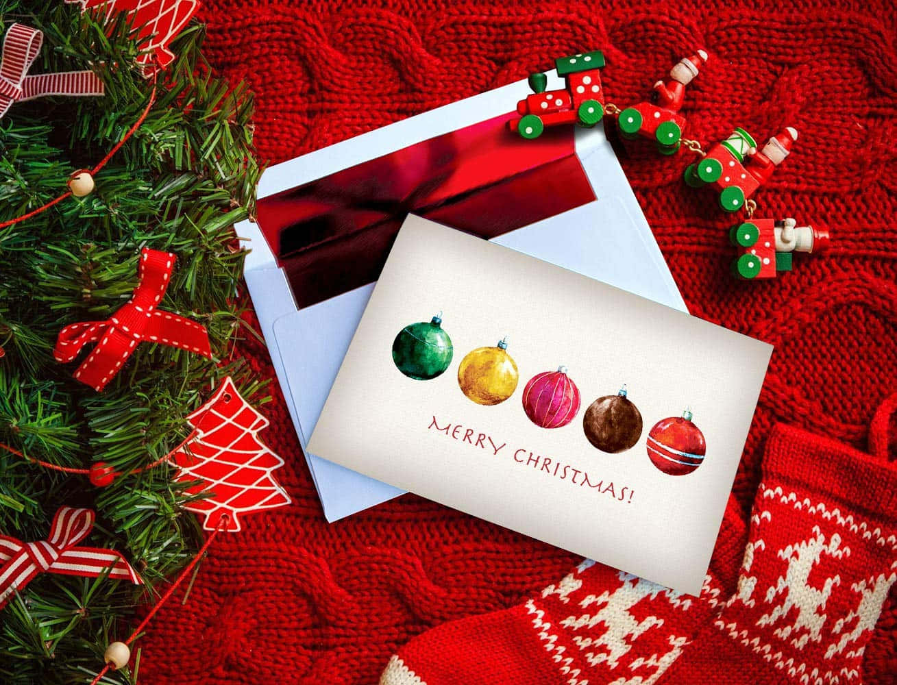 Christmas Card 桌布 壁紙 — 一張節日聖誕卡，上面有色彩繽紛的裝飾品，放在紅色針織毯上，旁邊有花環和節日裝飾。