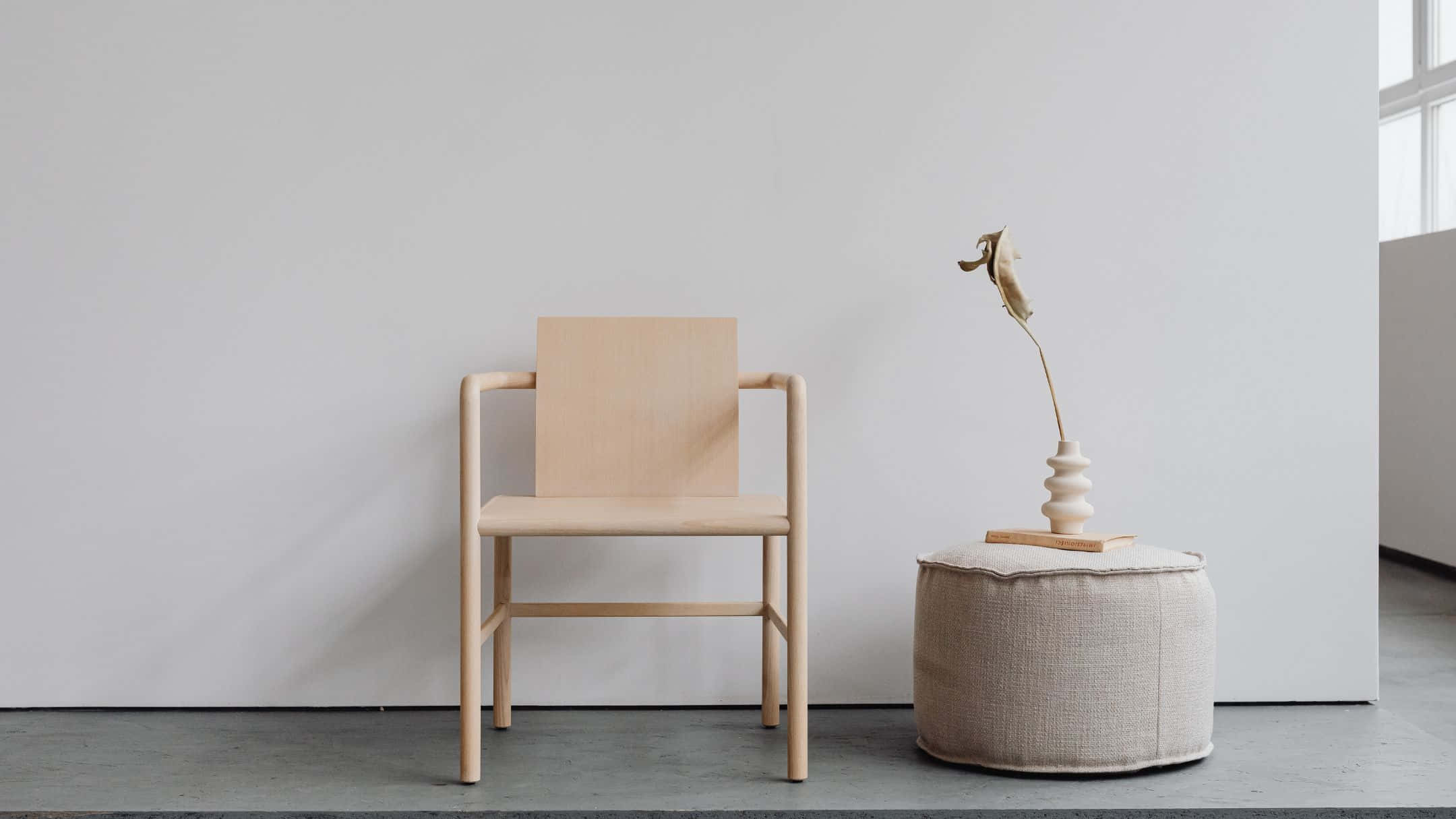 Furniture 桌布 壁紙 — 一張簡約木椅放在一張有質感的腳凳旁邊，腳凳上有一個陶瓷花瓶，插著乾花，靠近窗邊。