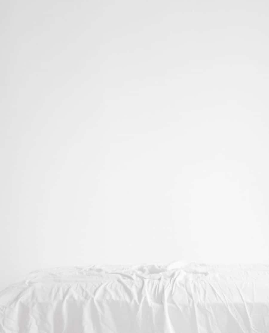 白色美學動圖 桌布 壁紙 — 一張簡約的白色床，床單皺褶，靠著純白牆壁，營造出寧靜整潔的空間。
