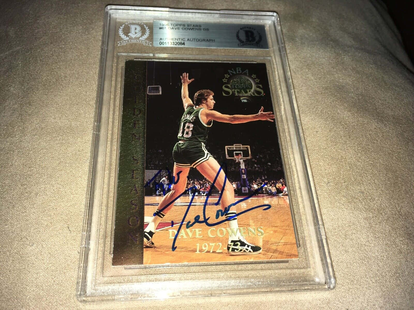 波士頓塞爾提克 桌布 壁紙 — 一張簽名的1994年Topps Stars Dave Cowens綠色球衣中距離投籃籃球卡，封裝在透明保護板中，放在米色布料表面上。