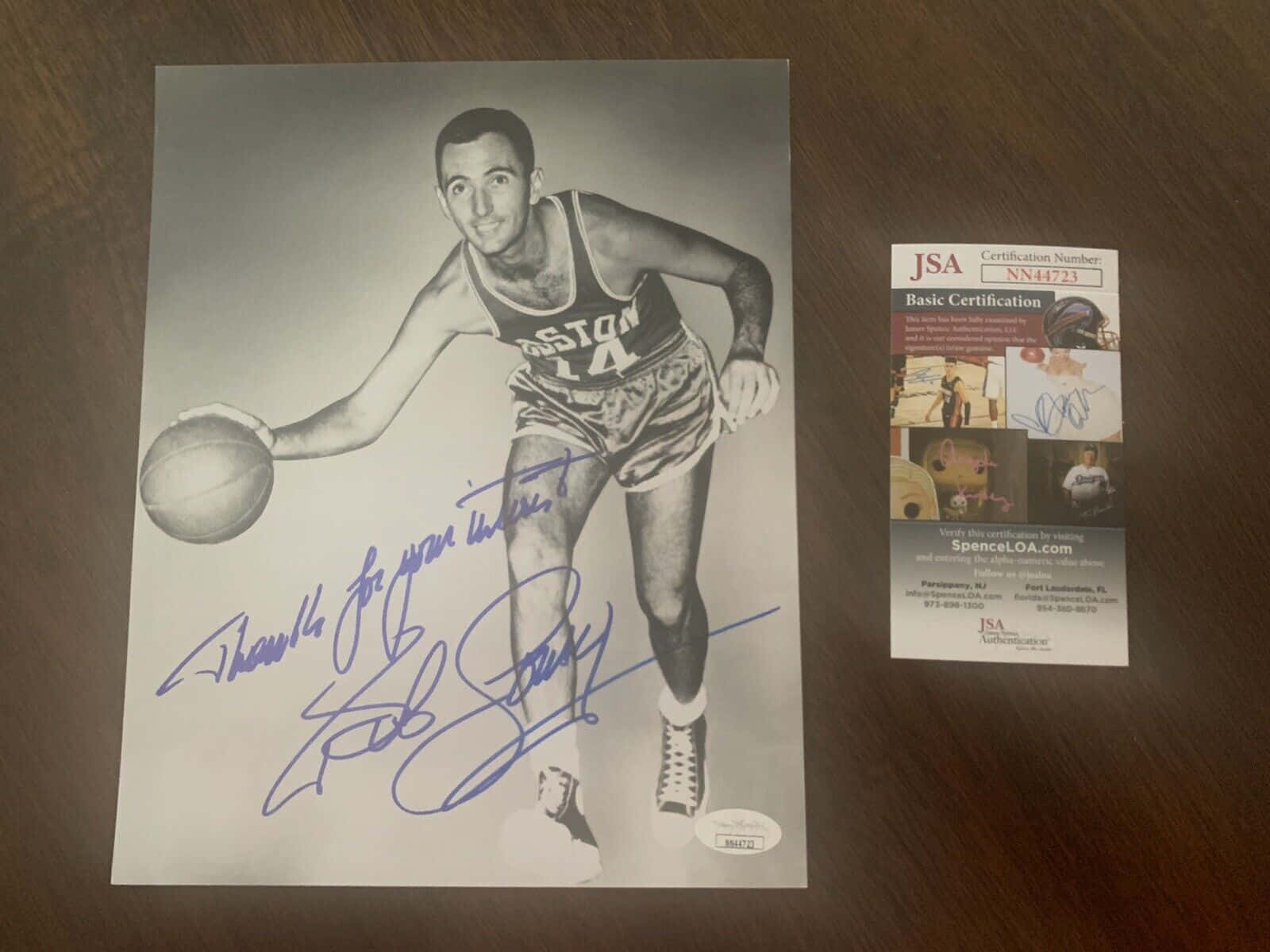 黑白 桌布 壁紙 — 一張簽名黑白照片，籃球運動員Bob Cousy身穿波士頓塞爾提克隊制服運球，旁邊有簽名和JSA認證卡在木質表面上。