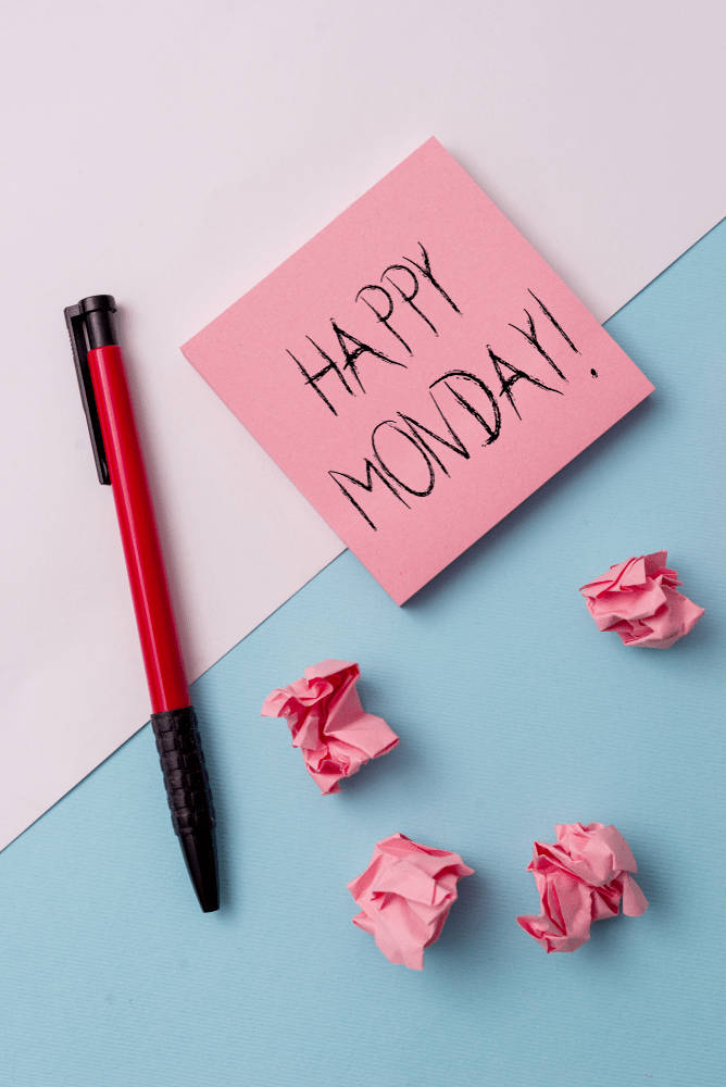 Happy Monday 桌布 壁紙 — 一張粉紅色便利貼寫著 'HAPPY MONDAY!'，旁邊有一支紅色筆和皺巴巴的粉紅色紙張，放在白色和藍色分半的表面上。