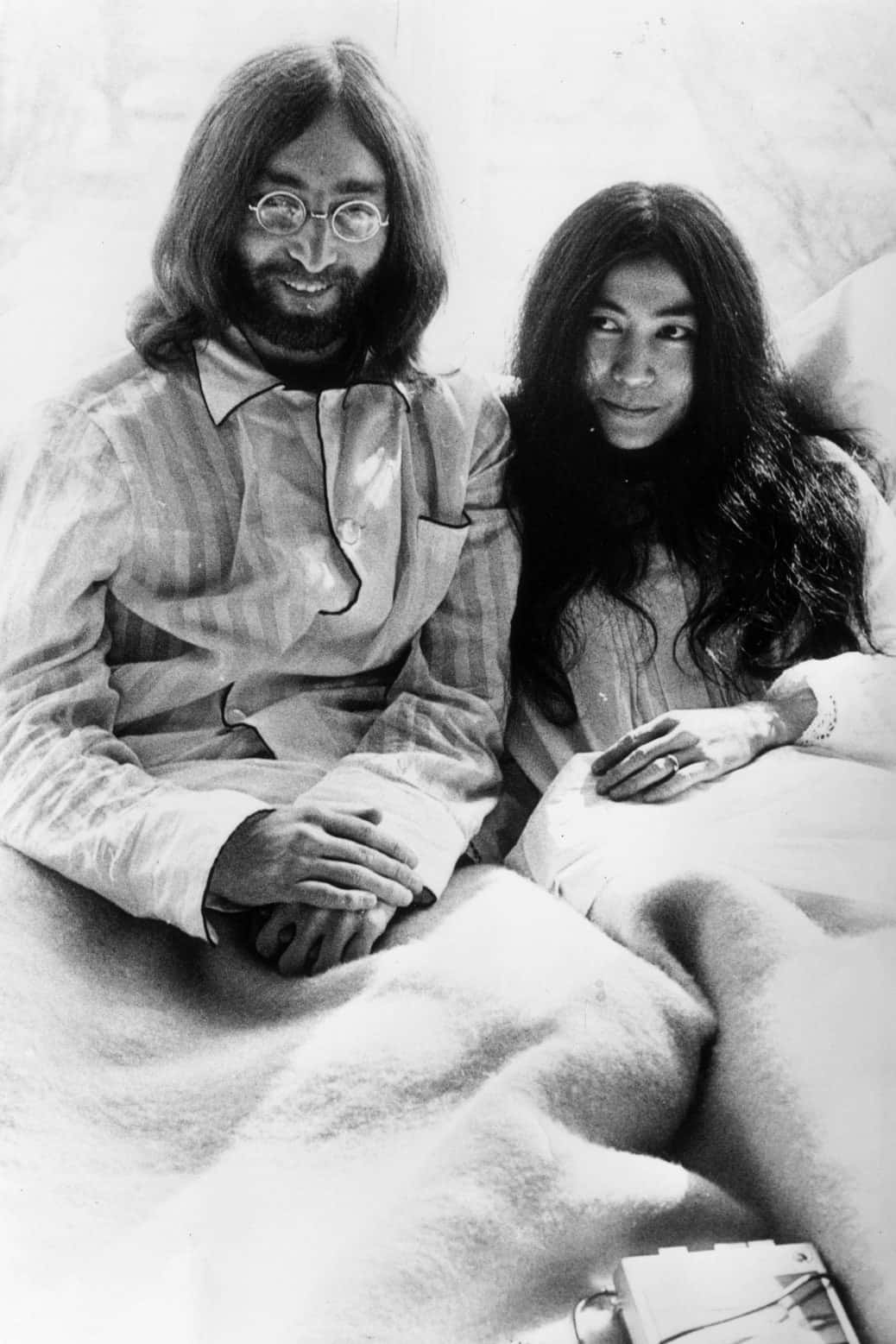 bed 桌布 壁紙 — 一張約翰·藍儂和小野洋子一起坐在鋪有毛絨毯子的床上的黑白照片。