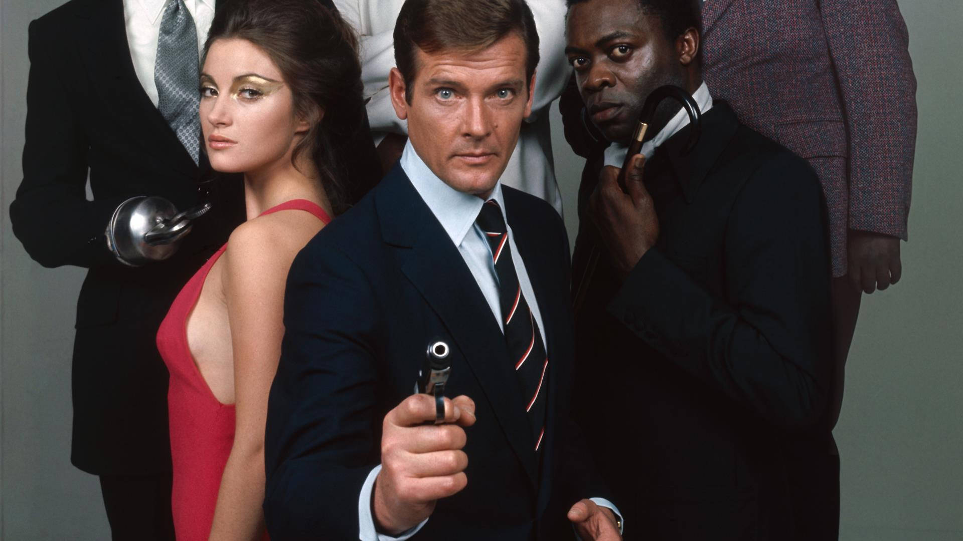 Yaphet Kotto 桌布 壁紙 — 一張緊張的1960年代間諜電影劇照，一名穿西裝的男子手持手槍，兩側是一名穿紅裙的女子和一名被槍指著頭的男子。