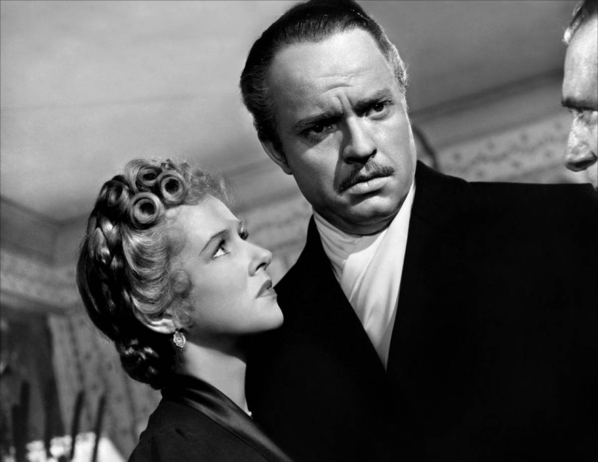Citizen Kane 桌布 壁紙 — 一張緊張的黑白場景顯示一名戴著髮捲的女子在室內仰望一位穿著西裝的嚴肅男子。