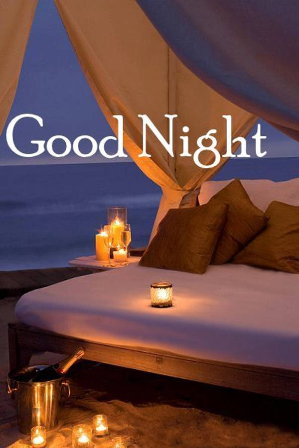 Good Night 桌布 壁紙 — 一張舒適的床，上方有垂墜布料，旁邊有發光的蠟燭和香檳桶，俯瞰黃昏時平靜的海洋。