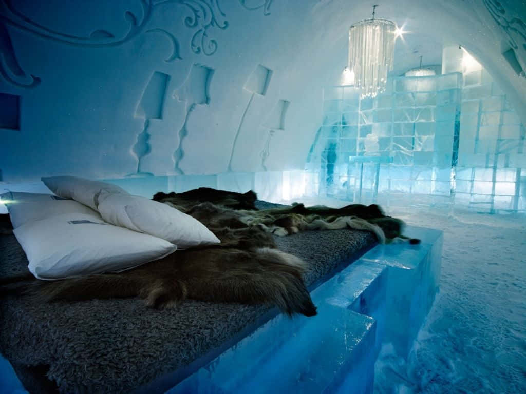 Ice Hotel 桌布 壁紙 — 一張舒適的床鋪，配有毛皮毯子和白色枕頭，放置在一個發光的藍色冰酒店房間的冰台上，房間有雕刻的牆壁和水晶吊燈。