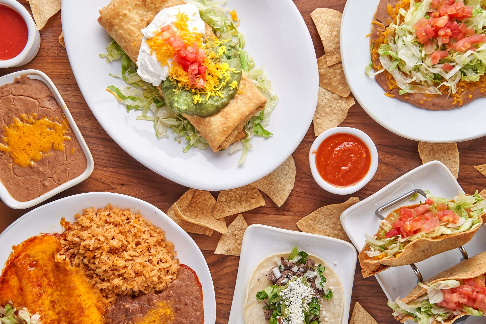 Mexican 桌布 壁紙 — 一張色彩繽紛的俯拍照片，展示各種墨西哥菜餚，包括玉米餅、捲餅和配菜，整齊擺放在木桌上。