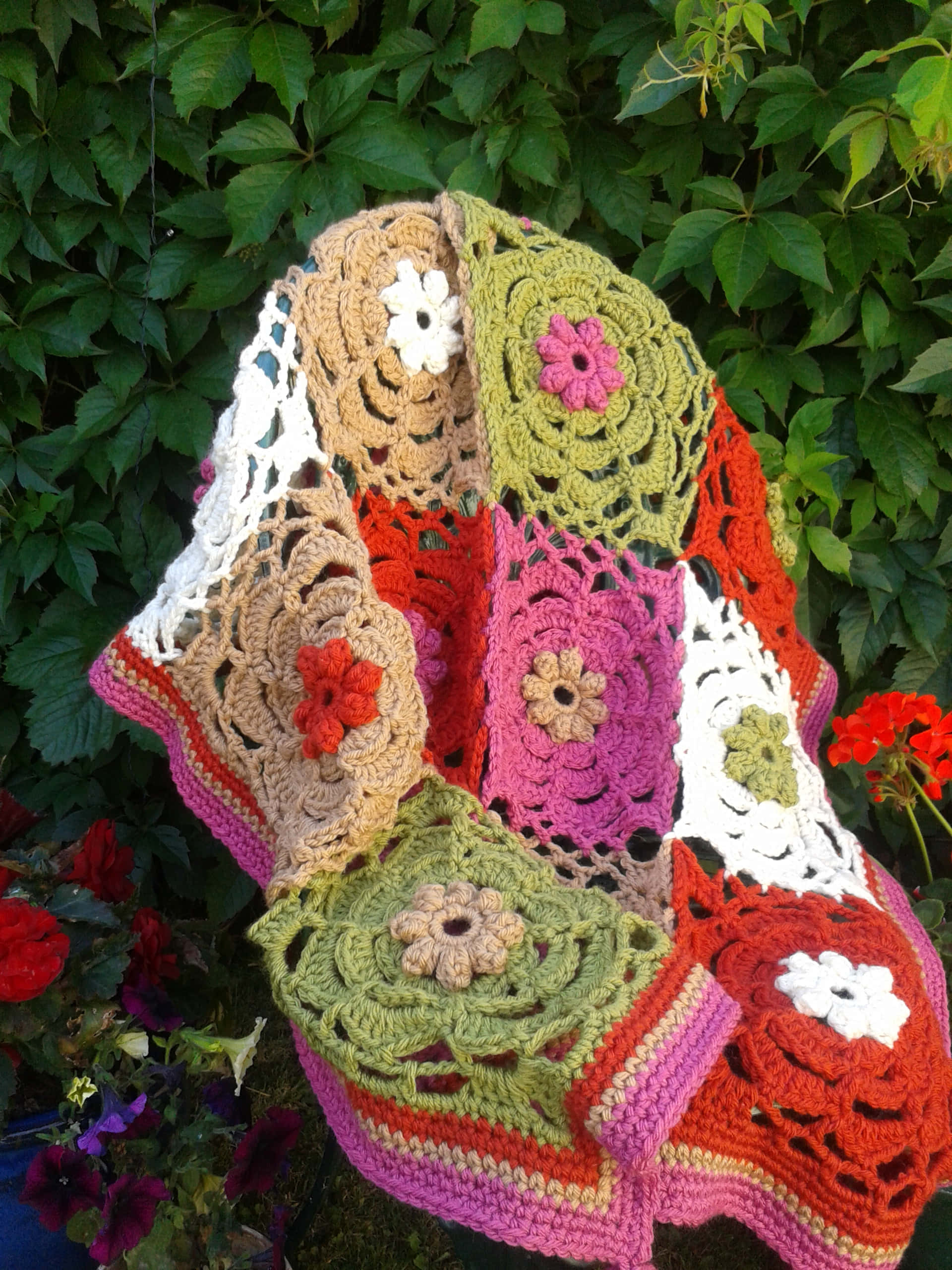 Blanket 桌布 壁紙 — 一張色彩繽紛的鉤針編織花卉圖案毯子，披在椅子上，背景是茂密的綠葉。