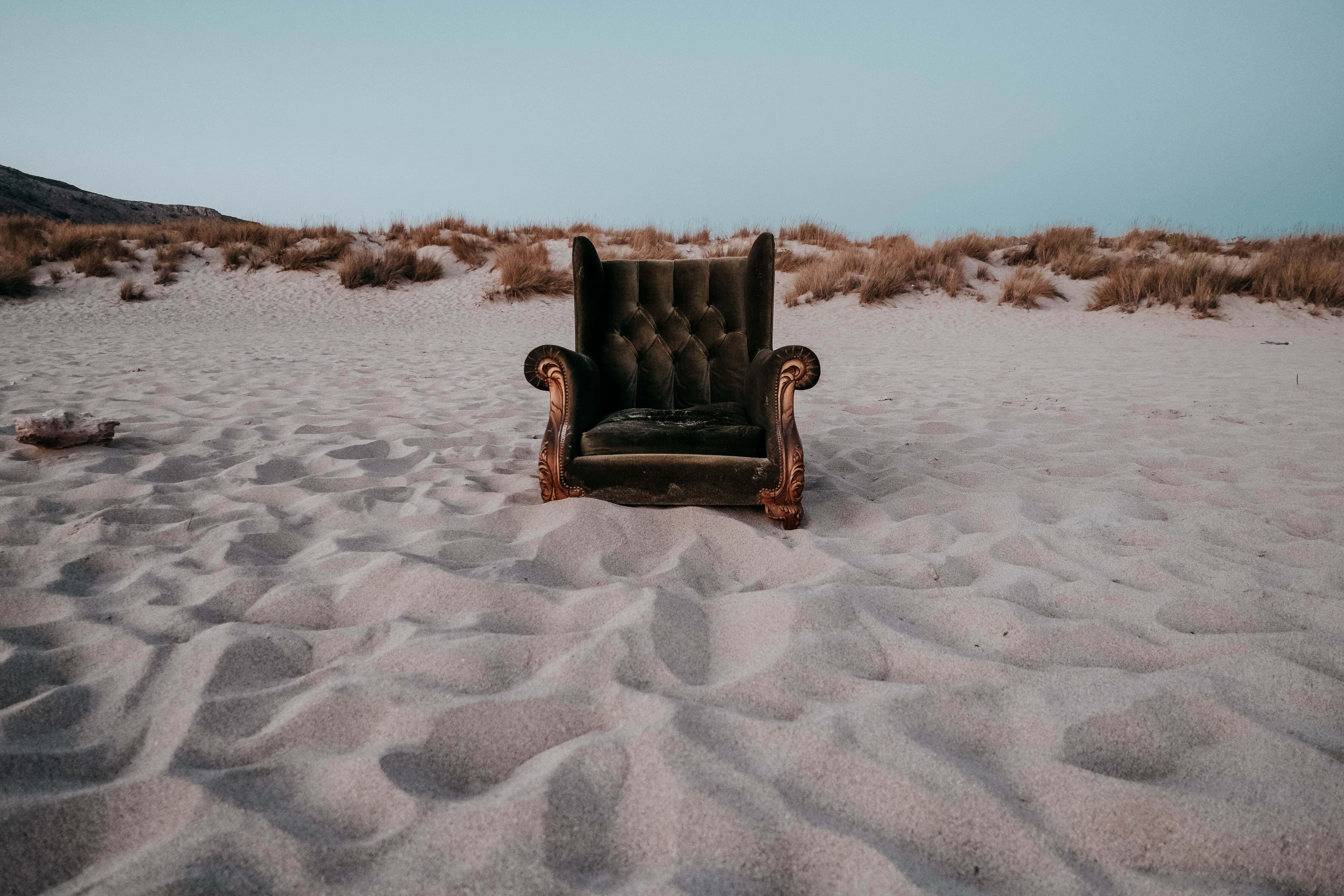 Aesthetic Beachy 桌布 壁紙 — 一張華麗的復古扶手椅獨自坐在廣闊的沙丘田野上，在柔和的暮色天空下。
