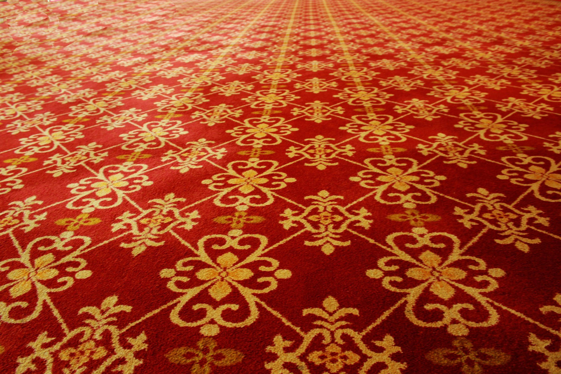 Red Carpet 桌布 壁紙 — 一張華麗的紅色地毯，帶有複雜的金色花卉圖案，以對稱、豪華的設計向外輻射。