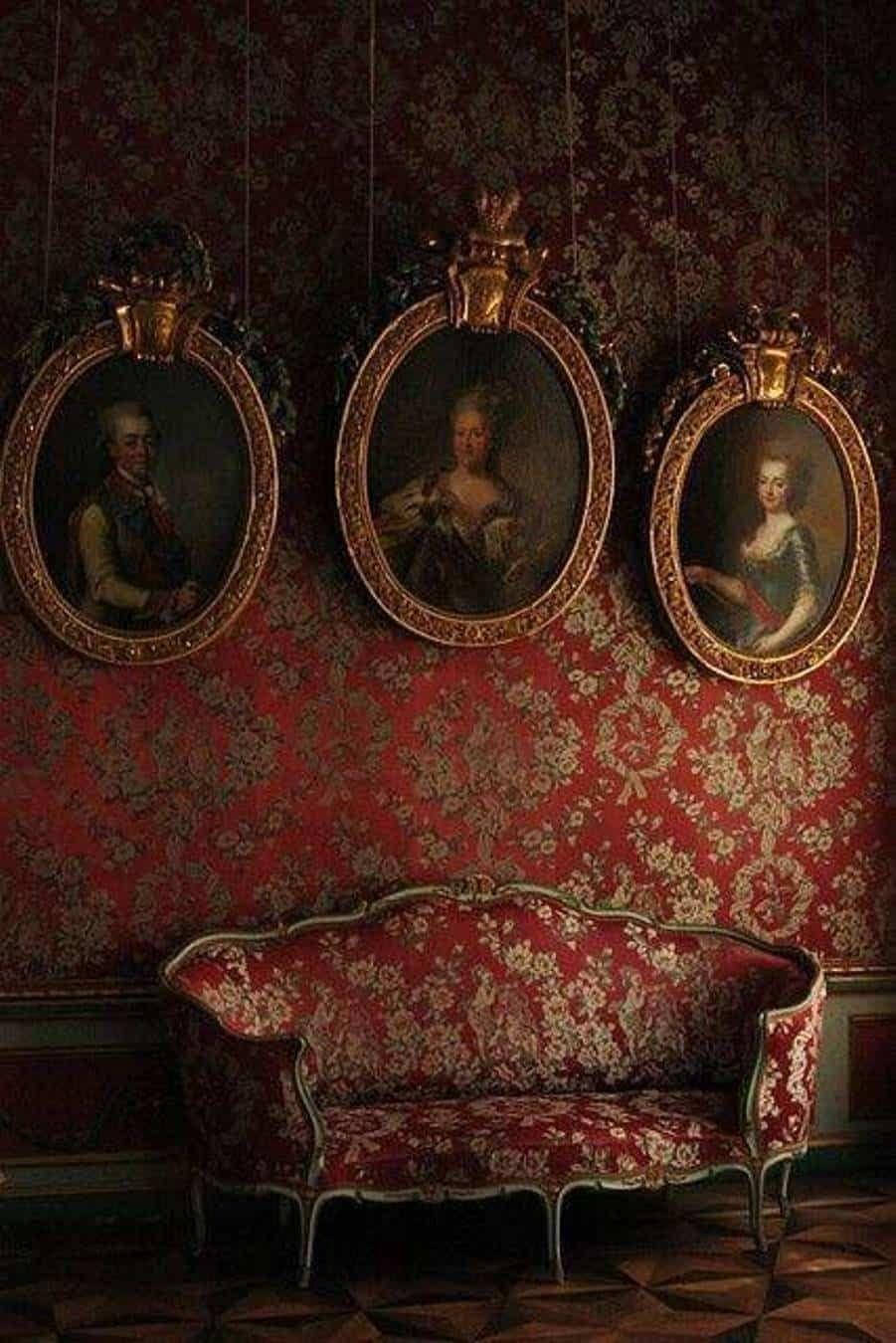 Victorian 桌布 壁紙 — 一張華麗的紅色錦緞沙發放在三幅懸掛的橢圓形畫像下方，處於燈光昏暗的豪華復古房間中。