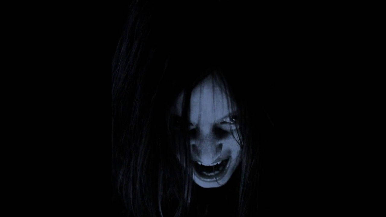 Scared 桌布 壁紙 — 一張蒼白的鬼臉，有著狂野的黑髮和寬闊的威脅笑容，在詭異的藍色燈光下從完全黑暗中浮現。