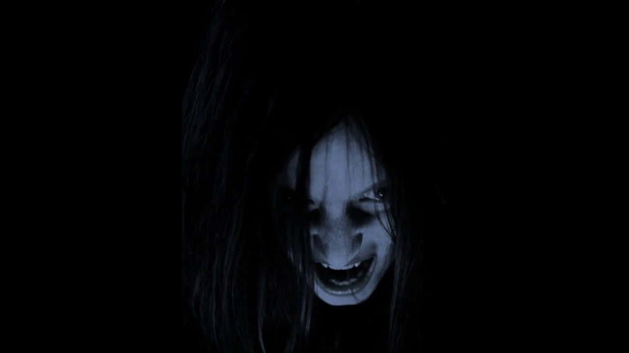 Dark Scary 桌布 壁紙 — 一張蒼白的鬼臉，有著狂野的黑髮和寬闊的威脅性笑容，在詭異的藍色燈光下從完全的黑暗中浮現。