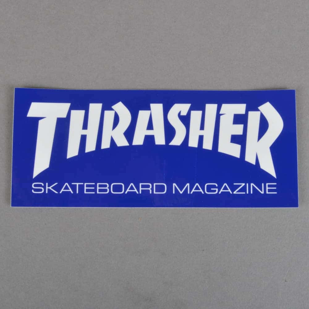 Thrasher 桌布 壁紙 — 一張藍色Thrasher Skateboard Magazine貼紙，帶有粗體白色文字，平放在純灰色表面上。